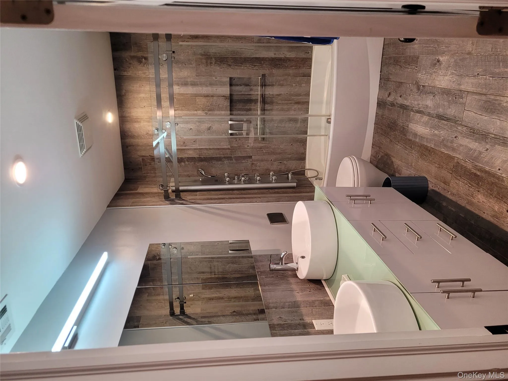 Bathroom featuring wood finished floors, enclosed tub / shower combo, and double vanity Bathroom featuring wood finished floors, enclosed tub / shower combo, and double vanity