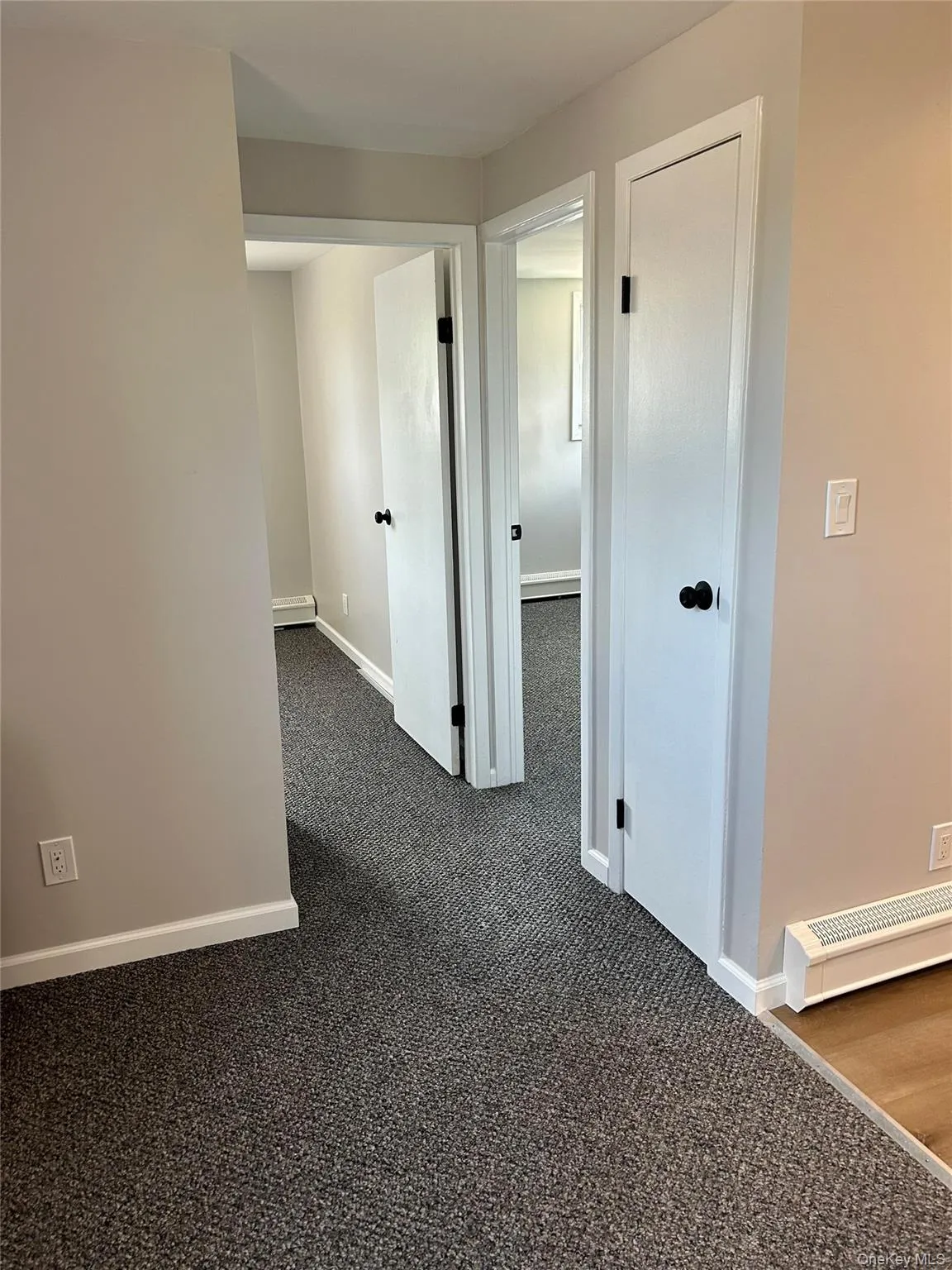 Corridor featuring dark colored carpet and baseboards Corridor featuring dark colored carpet and baseboards