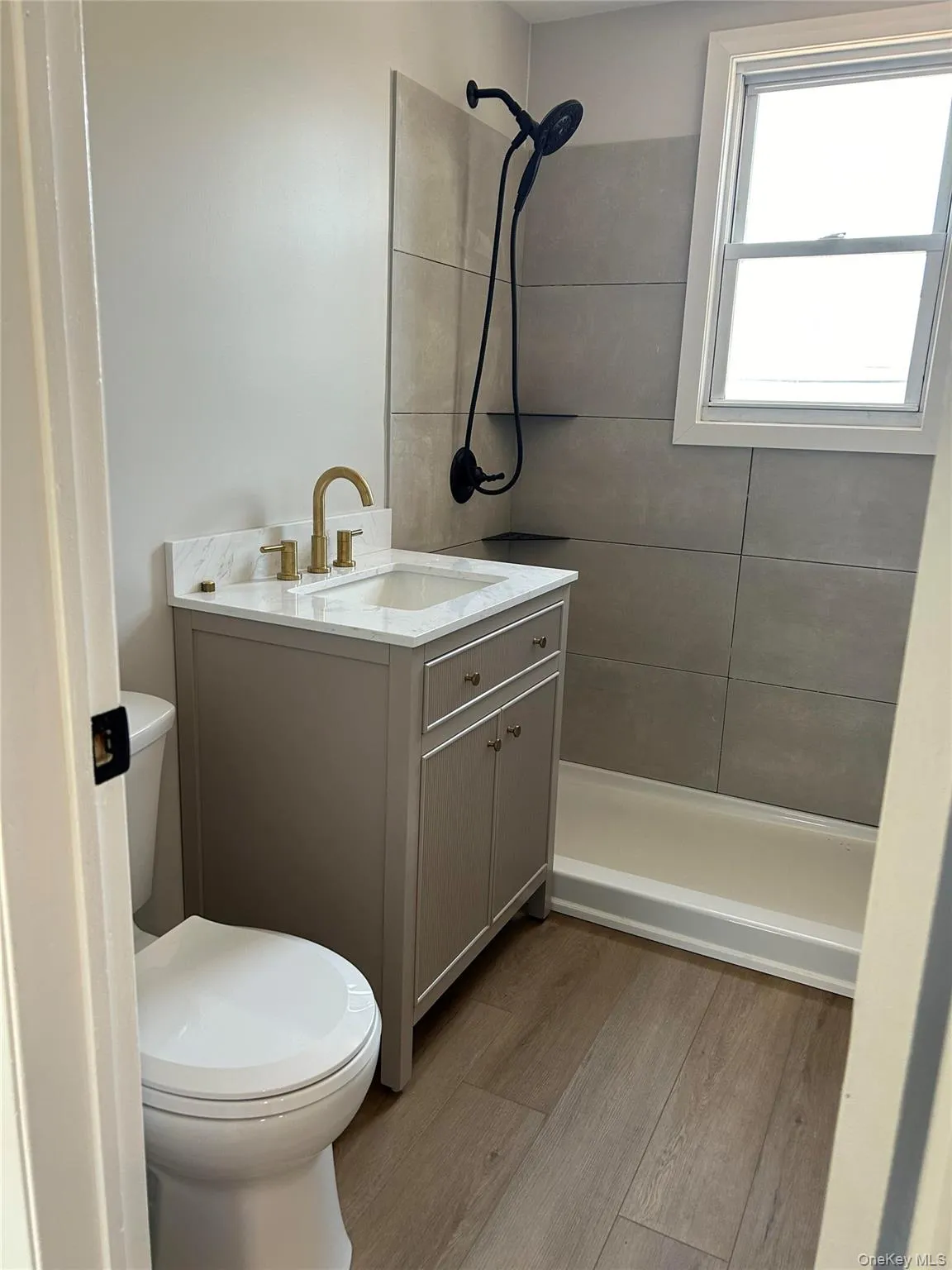 Bathroom featuring tiled shower, vanity, and wood finished floors Bathroom featuring tiled shower, vanity, and wood finished floors