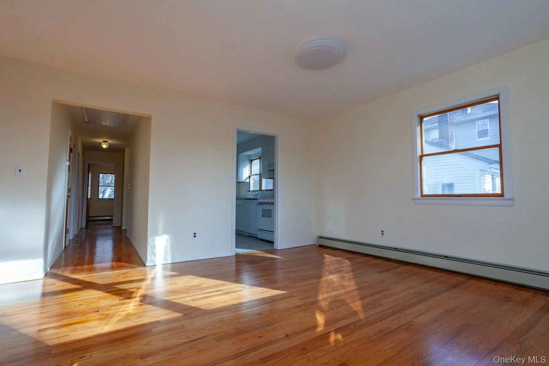 Unfurnished living room with hardwood floors, access to kitchen and baseboard heating. Unfurnished living room with hardwood floors, access to kitchen and baseboard heating.