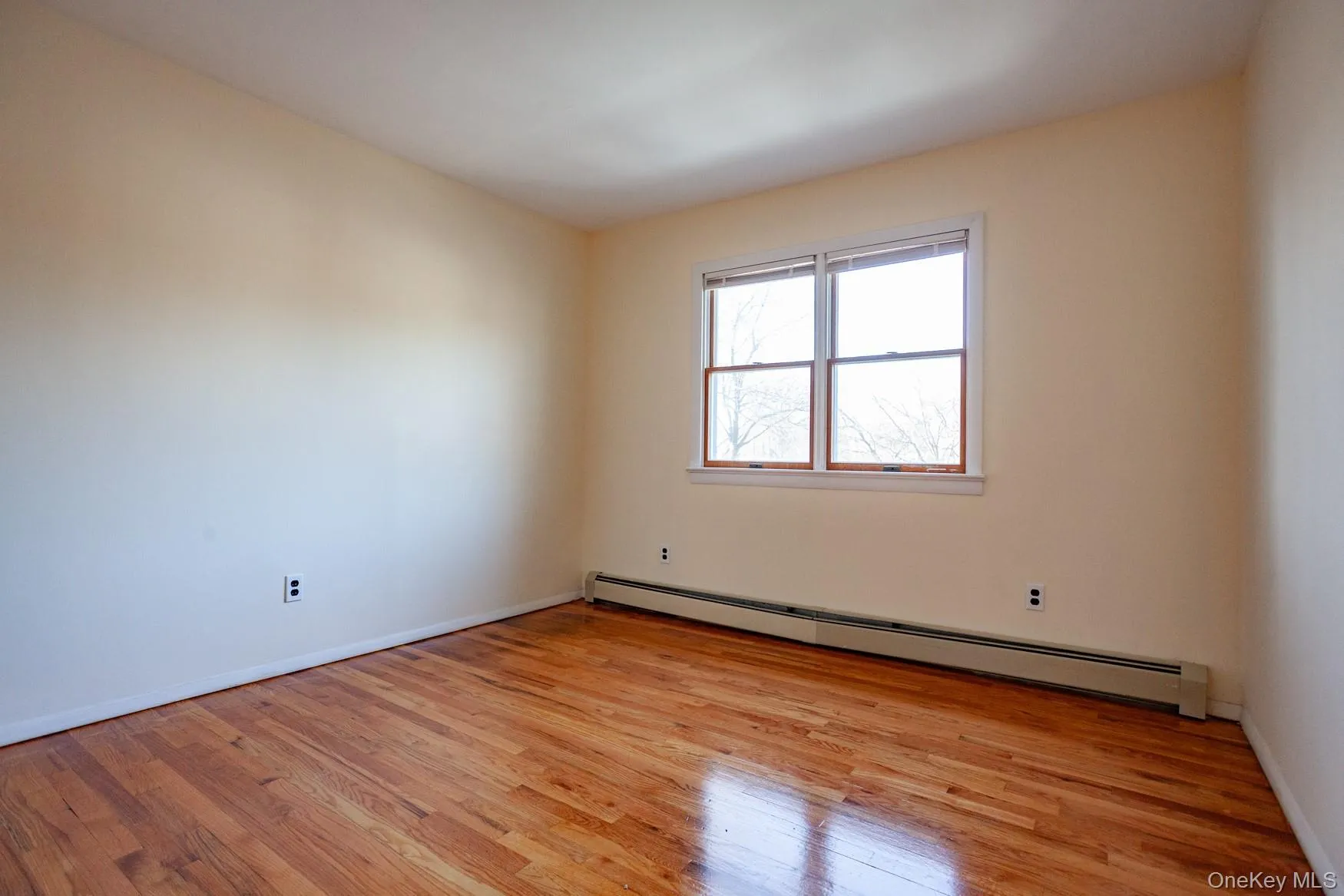 Unfurnished room with a baseboard radiator and light hardwood flooring. Unfurnished room with a baseboard radiator and light hardwood flooring.