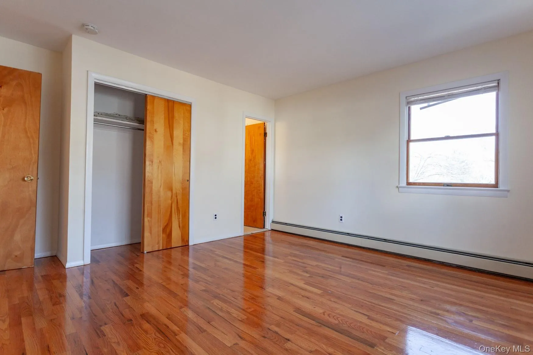 Unfurnished bedroom with hardwood floors, baseboard heating, a spacious closet and access to primary bathroom. Unfurnished bedroom with hardwood floors, baseboard heating, a spacious closet and access to primary bathroom.