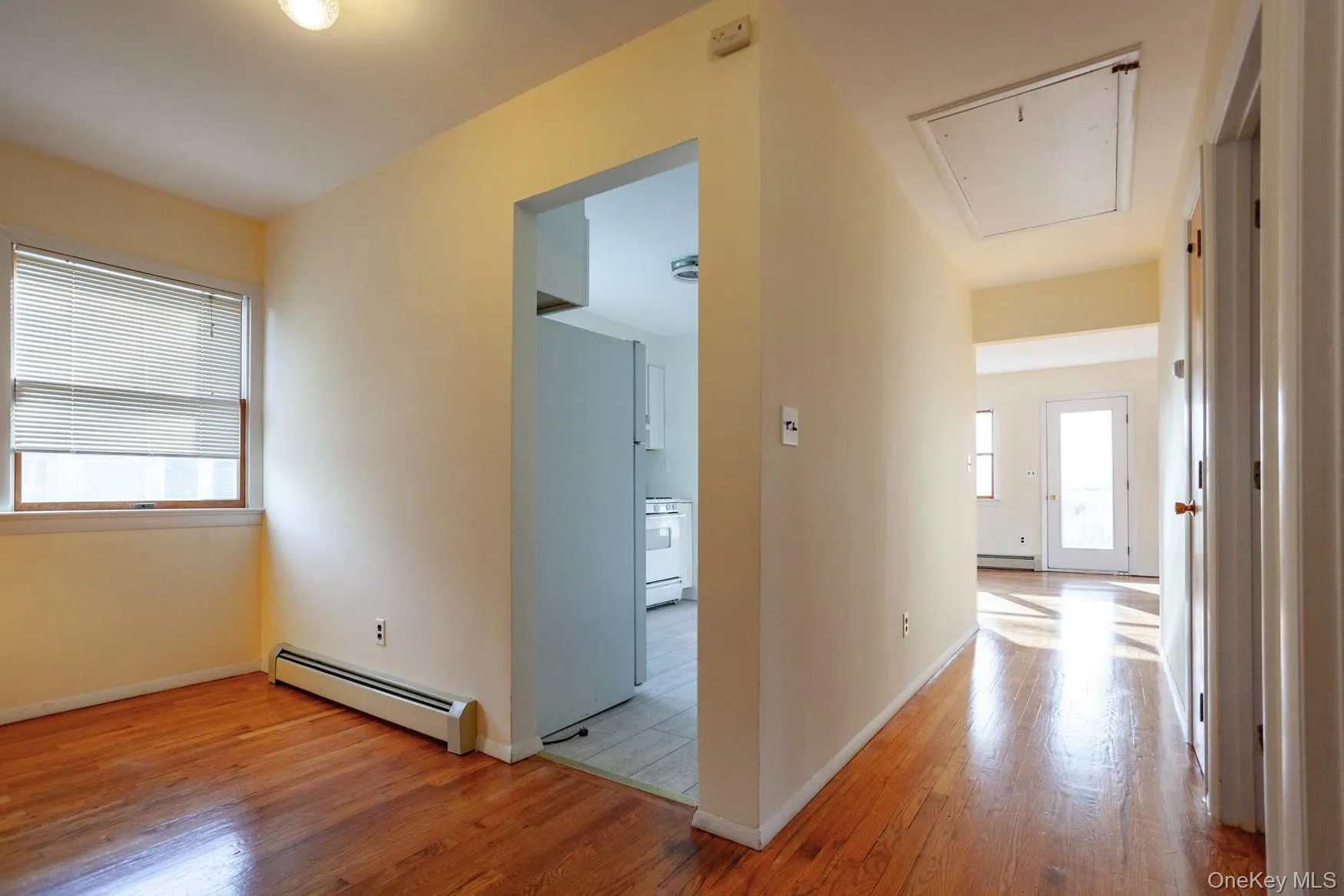 Hallway featuring light hardwood flooring, entry to the kitchen and attic access. Hallway featuring light hardwood flooring, entry to the kitchen and attic access.