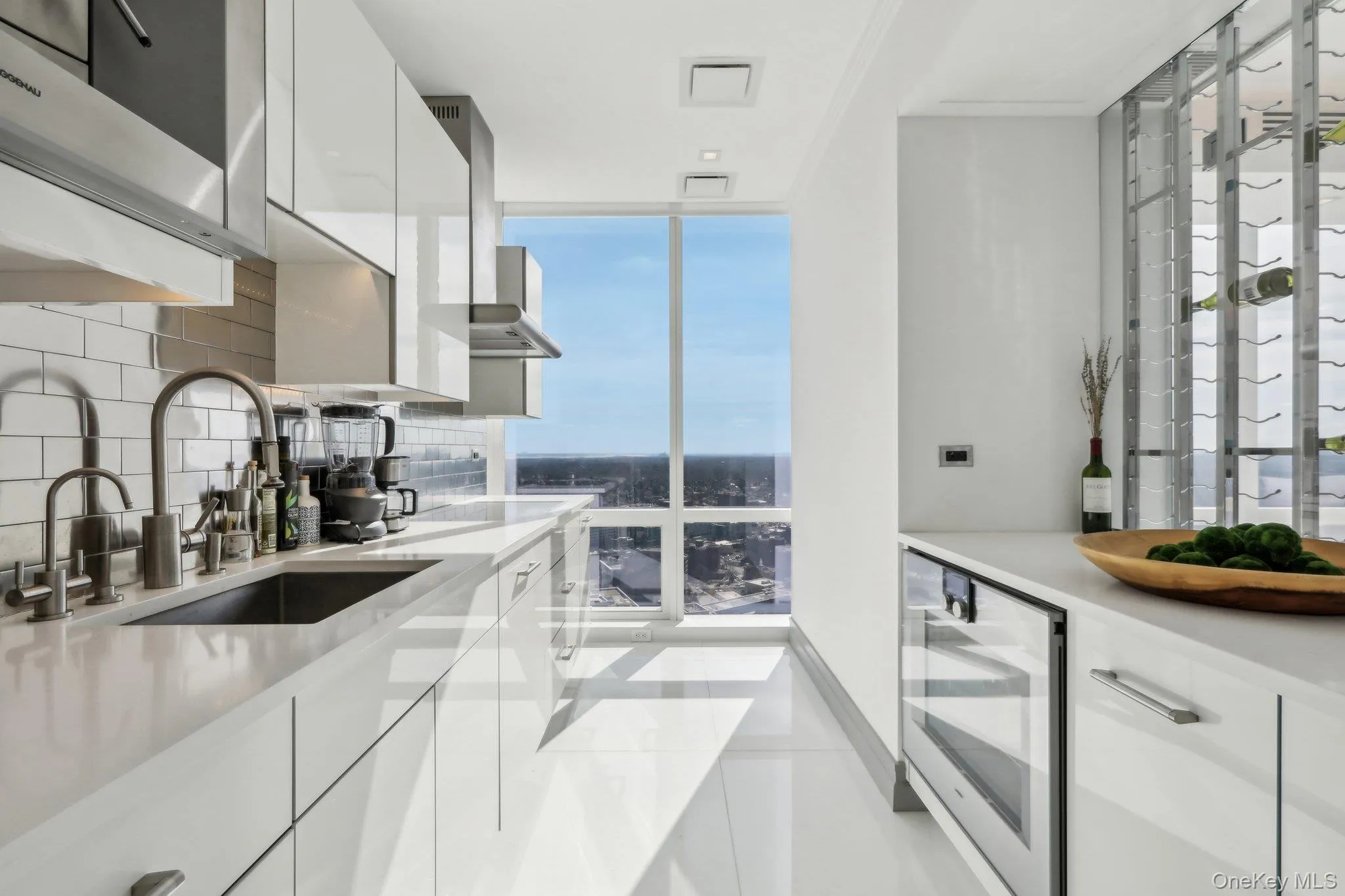 Kitchen featuring modern cabinets, wine cooler, decorative backsplash, white cabinetry, and light countertops Kitchen featuring modern cabinets, wine cooler, decorative backsplash, white cabinetry, and light countertops