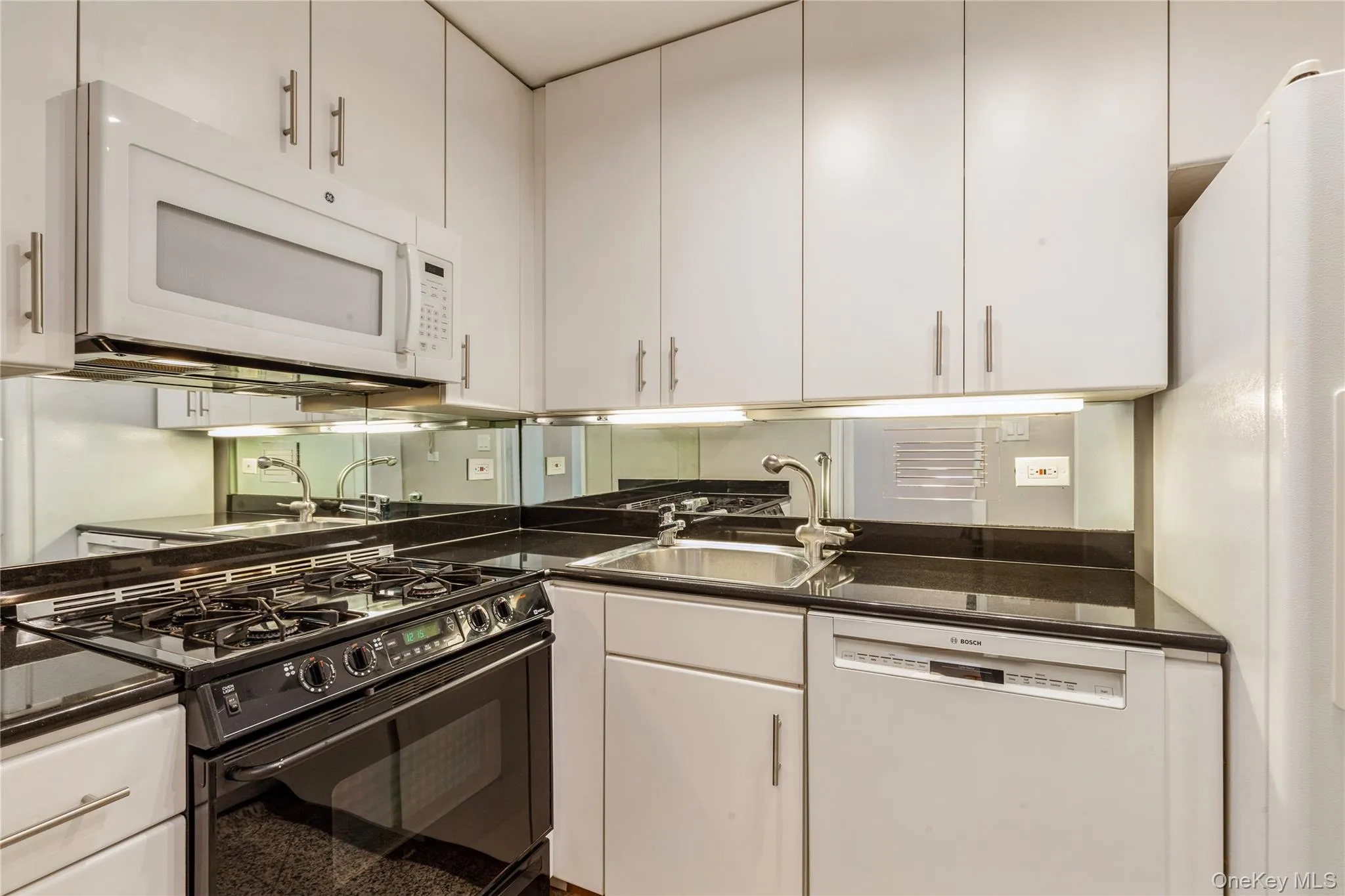 Kitchen with white appliances, white cabinetry, and dark countertops Kitchen with white appliances, white cabinetry, and dark countertops