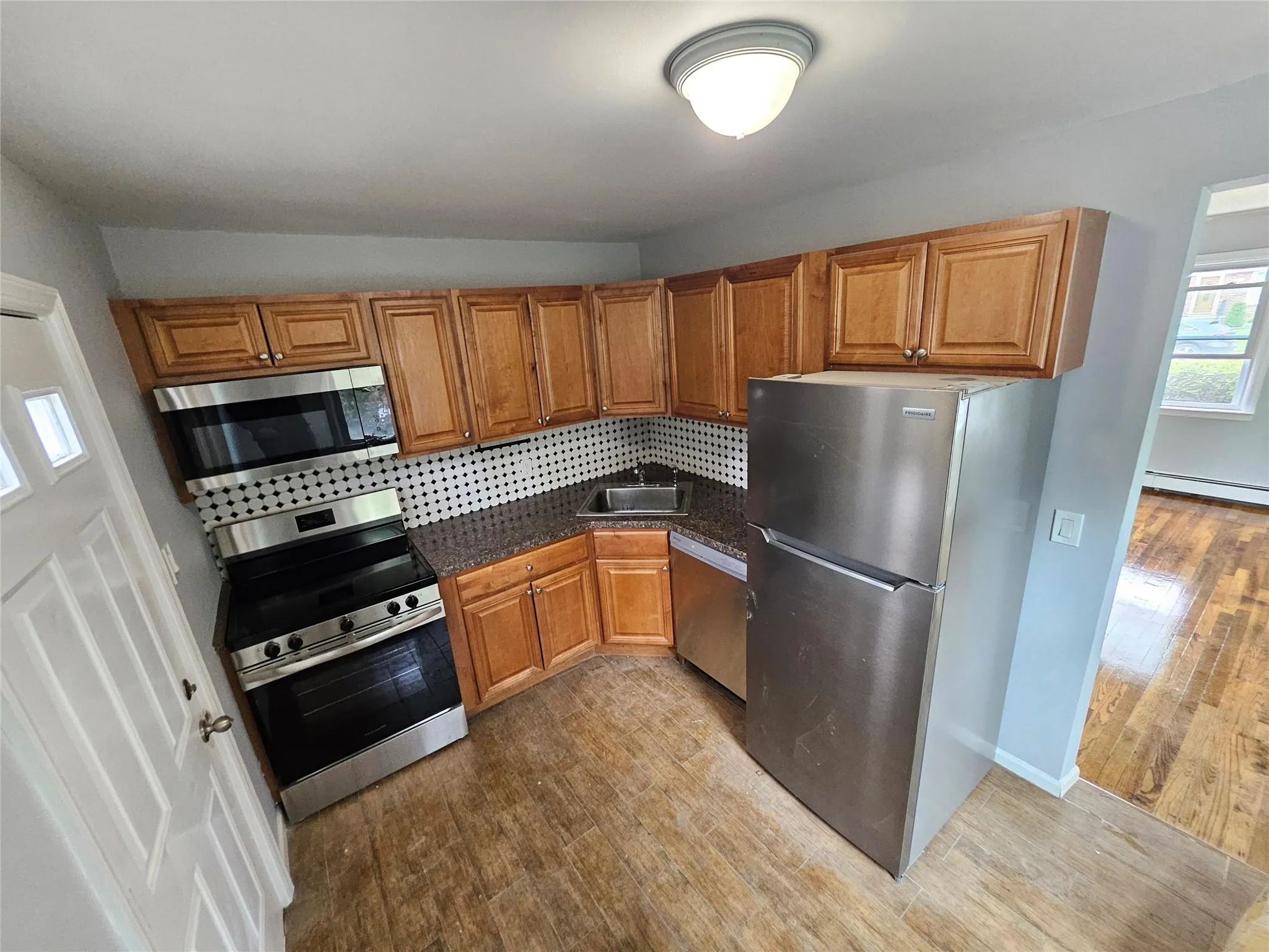 Kitchen with stainless steel appliances, wood finished floors, dark countertops, brown cabinets, and backsplash Kitchen with stainless steel appliances, wood finished floors, dark countertops, brown cabinets, and backsplash