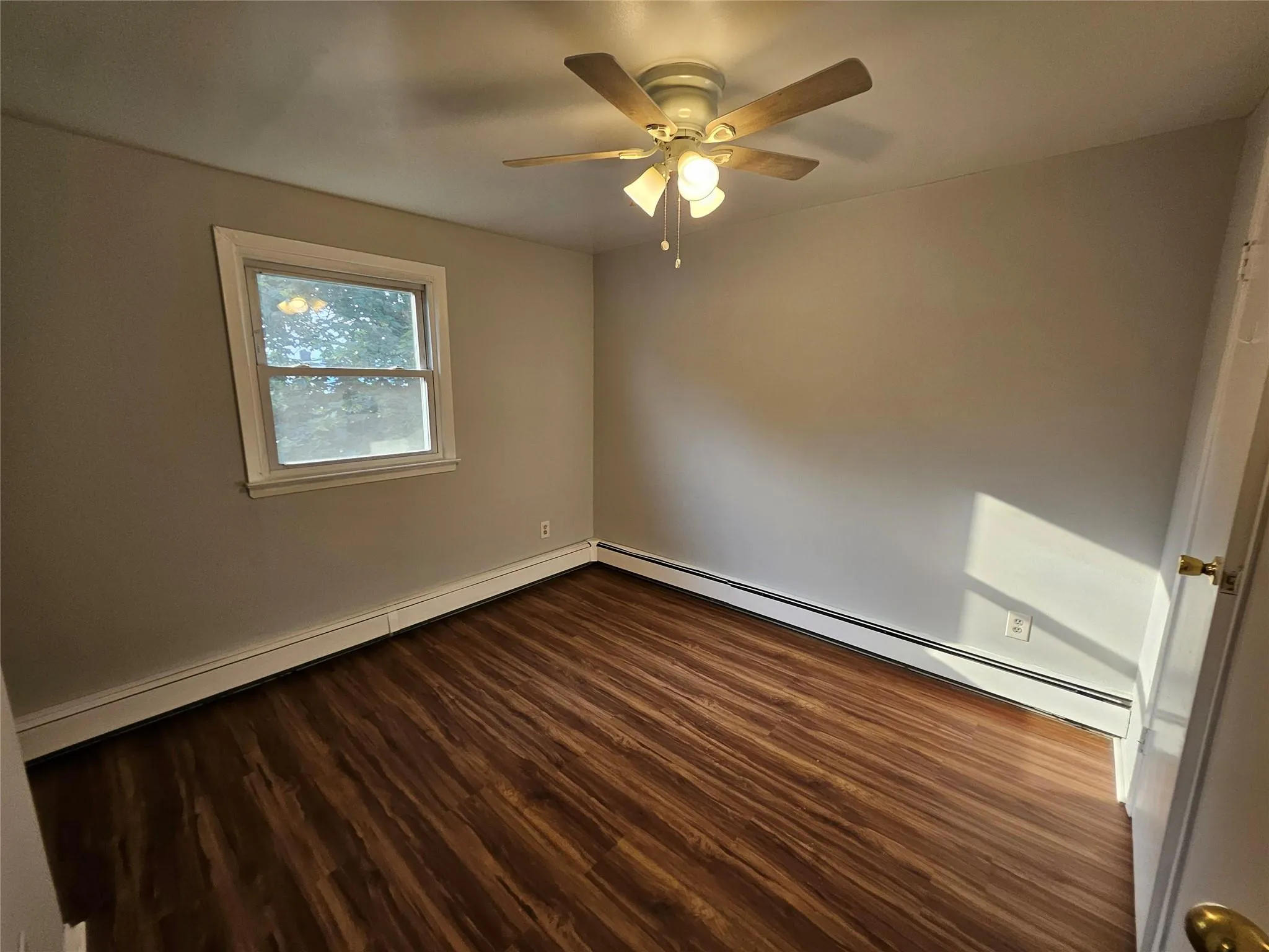 Empty room with dark wood-style flooring, a ceiling fan, a baseboard radiator, and baseboard heating Empty room with dark wood-style flooring, a ceiling fan, a baseboard radiator, and baseboard heating