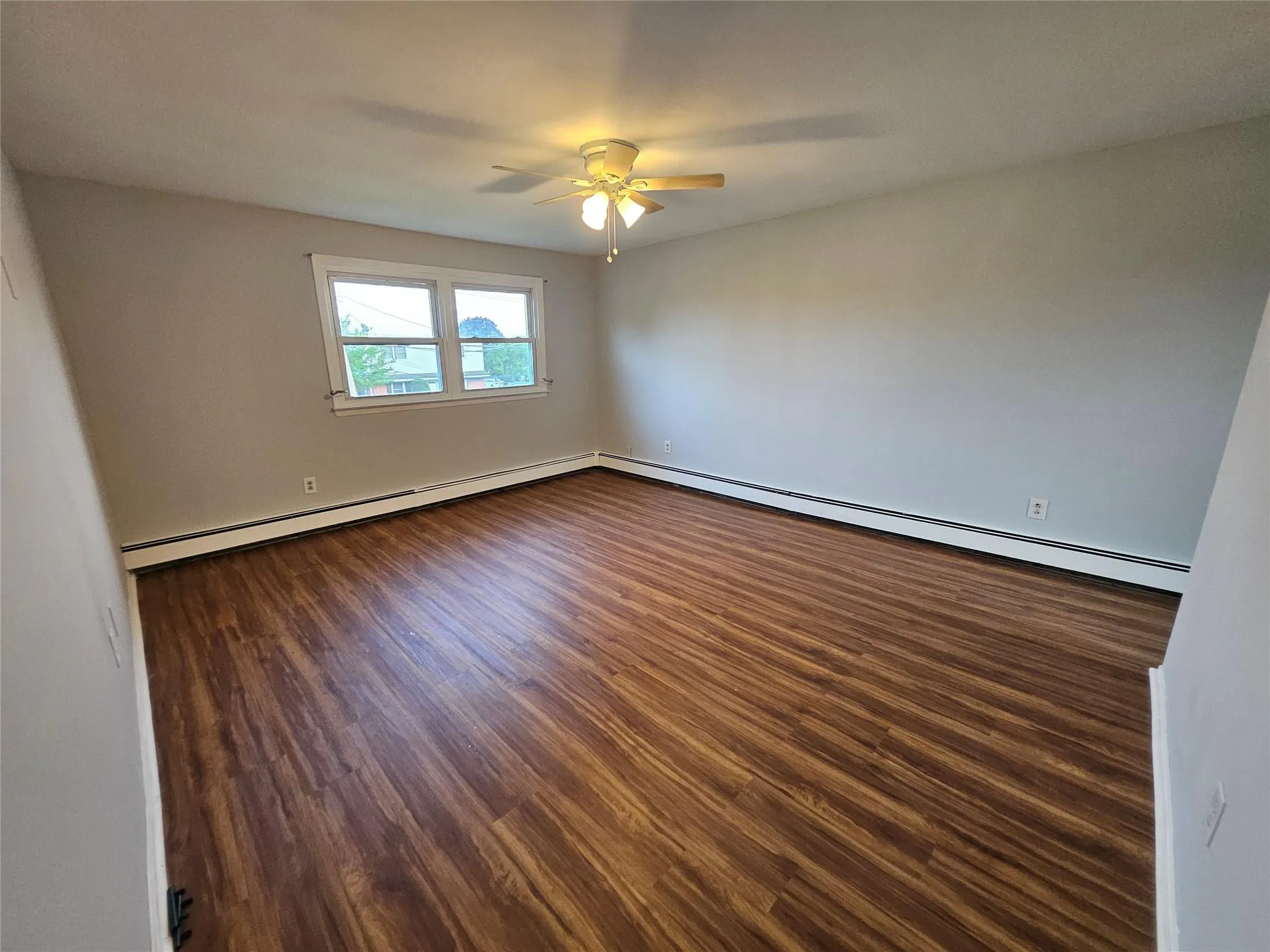 Spare room with a baseboard radiator, a ceiling fan, and dark wood-style floors Spare room with a baseboard radiator, a ceiling fan, and dark wood-style floors