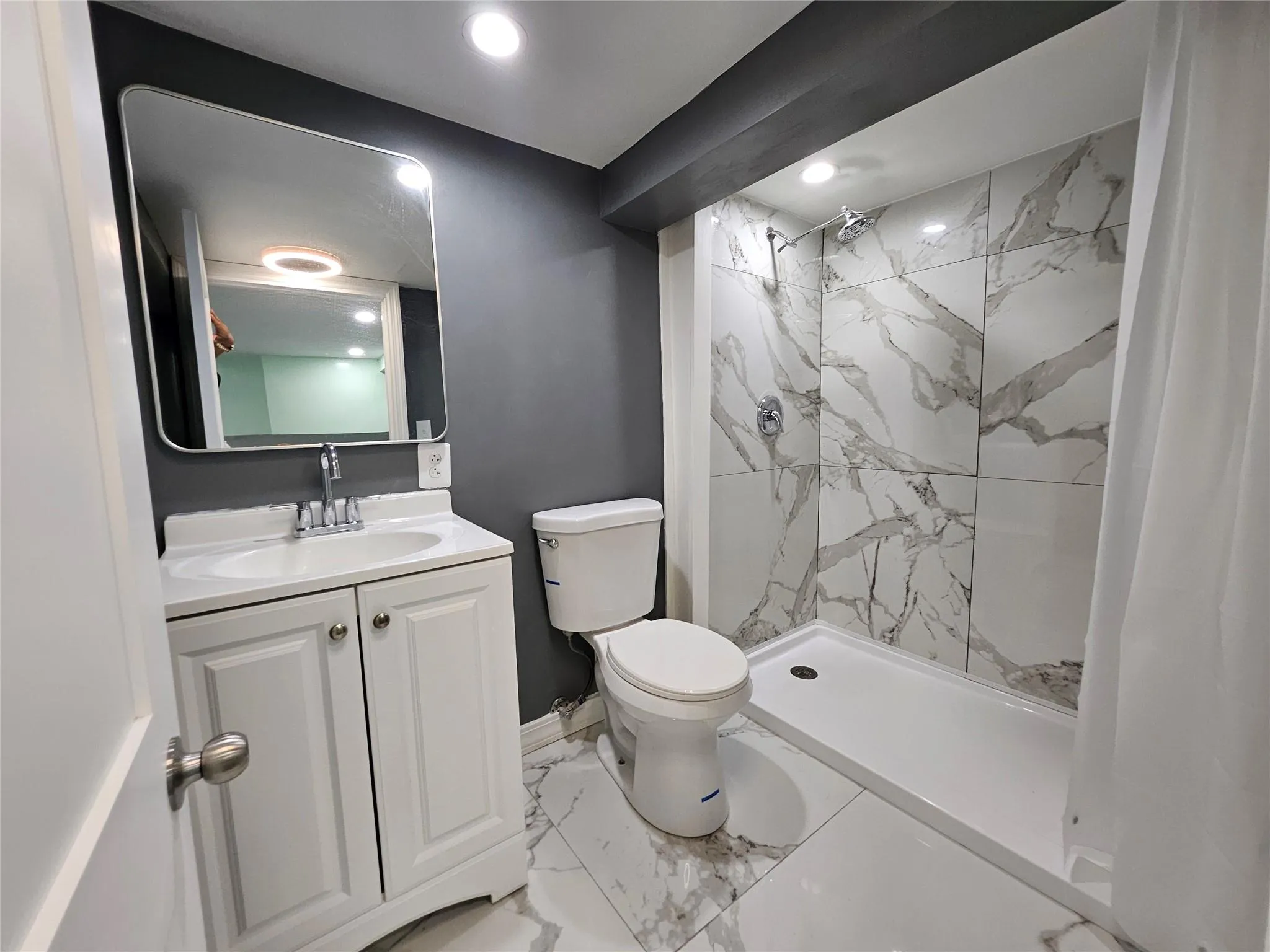 Full bathroom featuring marble look tiles, a marble finish shower, vanity, and recessed lighting Full bathroom featuring marble look tiles, a marble finish shower, vanity, and recessed lighting