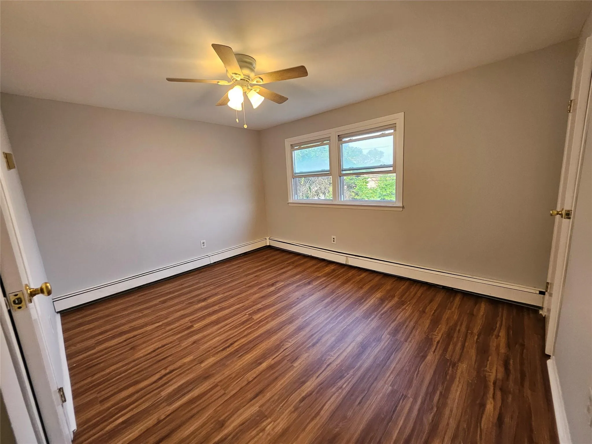 Spare room featuring dark wood-style flooring, ceiling fan, baseboard heating, and a baseboard heating unit Spare room featuring dark wood-style flooring, ceiling fan, baseboard heating, and a baseboard heating unit