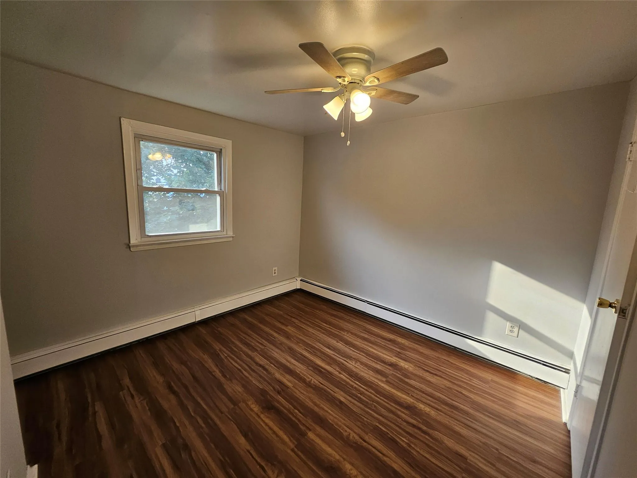 Unfurnished room with dark wood-type flooring, ceiling fan, and baseboard heating Unfurnished room with dark wood-type flooring, ceiling fan, and baseboard heating