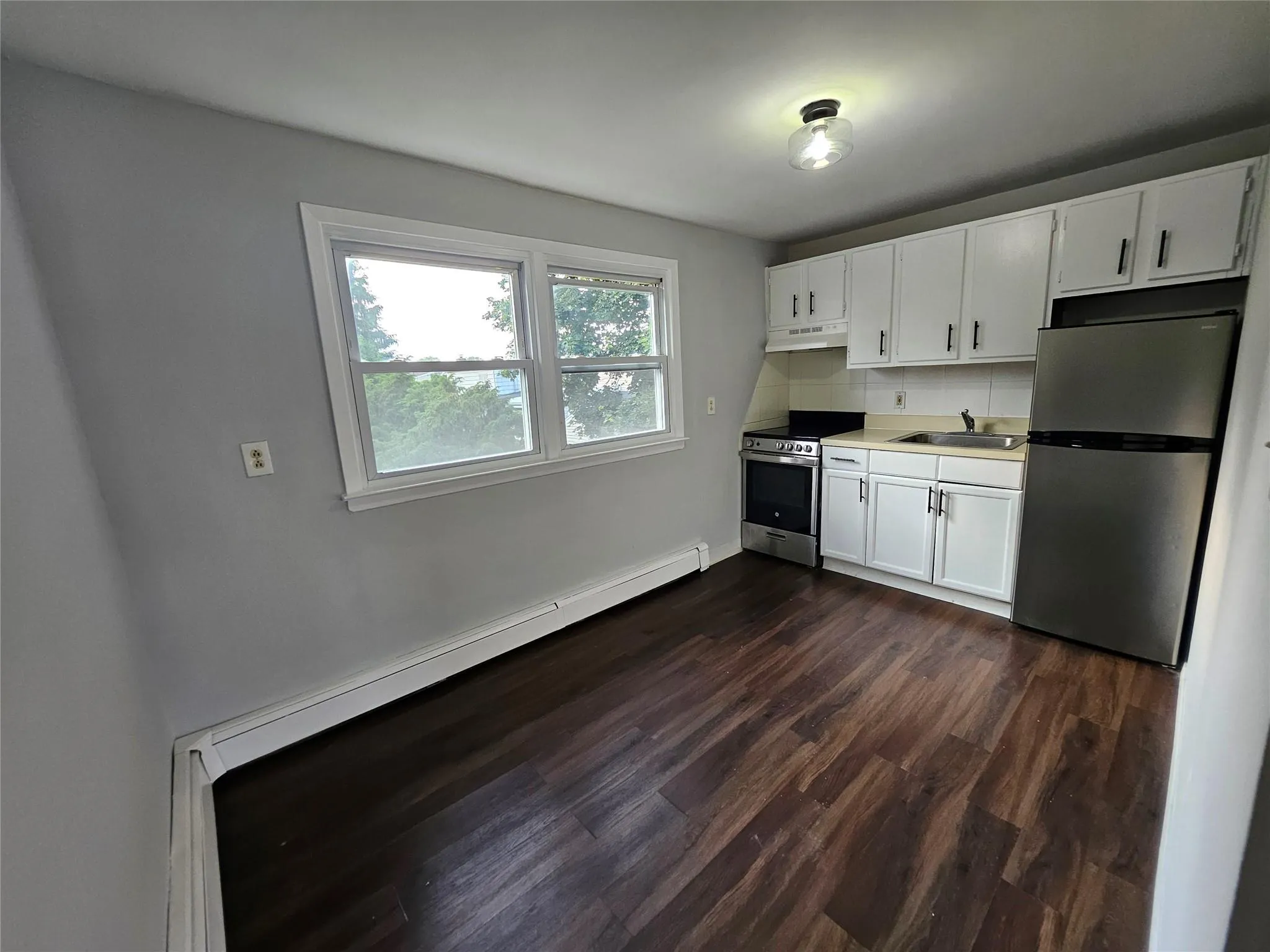Kitchen featuring stainless steel appliances, under cabinet range hood, dark wood finished floors, white cabinetry, and light countertops Kitchen featuring stainless steel appliances, under cabinet range hood, dark wood finished floors, white cabinetry, and light countertops