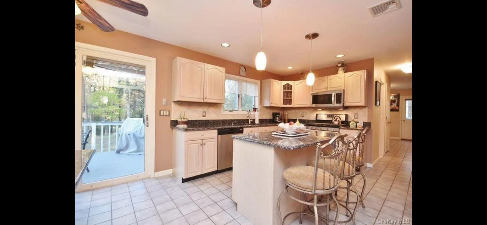 Kitchen featuring stainless steel appliances, a kitchen island, a kitchen bar, light tile patterned floors, and decorative light fixtures Kitchen featuring stainless steel appliances, a kitchen island, a kitchen bar, light tile patterned floors, and decorative light fixtures