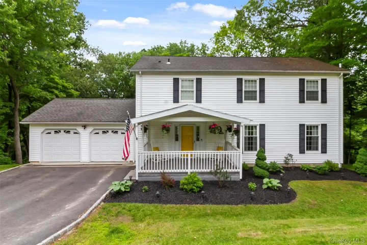Colonial inspired home featuring covered porch, driveway, an attached garage, and a front lawn