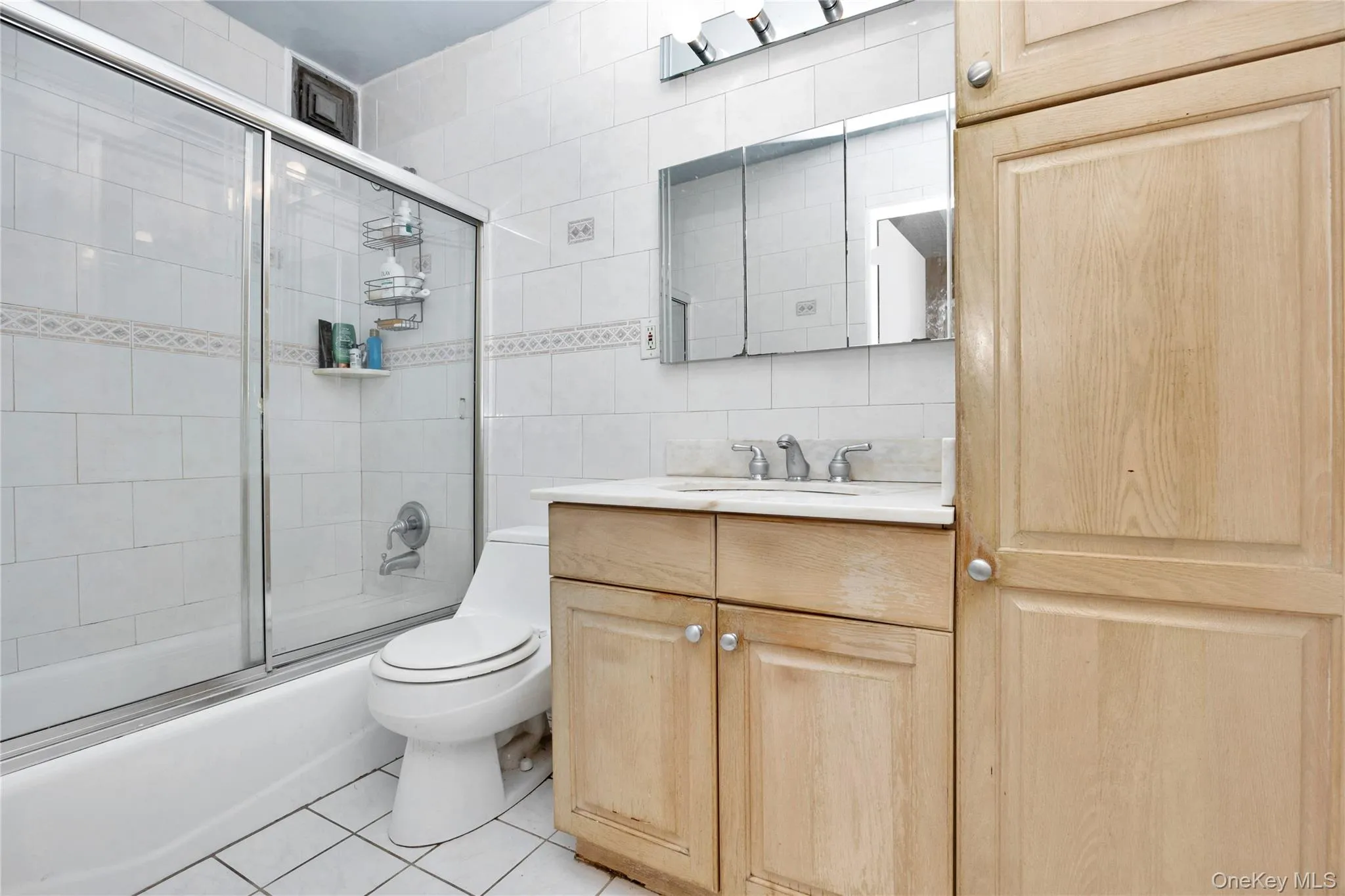 Full bath featuring vanity, tile patterned floors, tile walls, shower / bath combination with glass door, and backsplash Full bath featuring vanity, tile patterned floors, tile walls, shower / bath combination with glass door, and backsplash