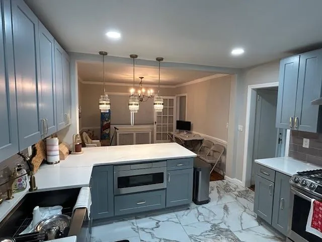 Kitchen with appliances with stainless steel finishes, a peninsula, light countertops, crown molding, and light marble finish flooring Kitchen with appliances with stainless steel finishes, a peninsula, light countertops, crown molding, and light marble finish flooring