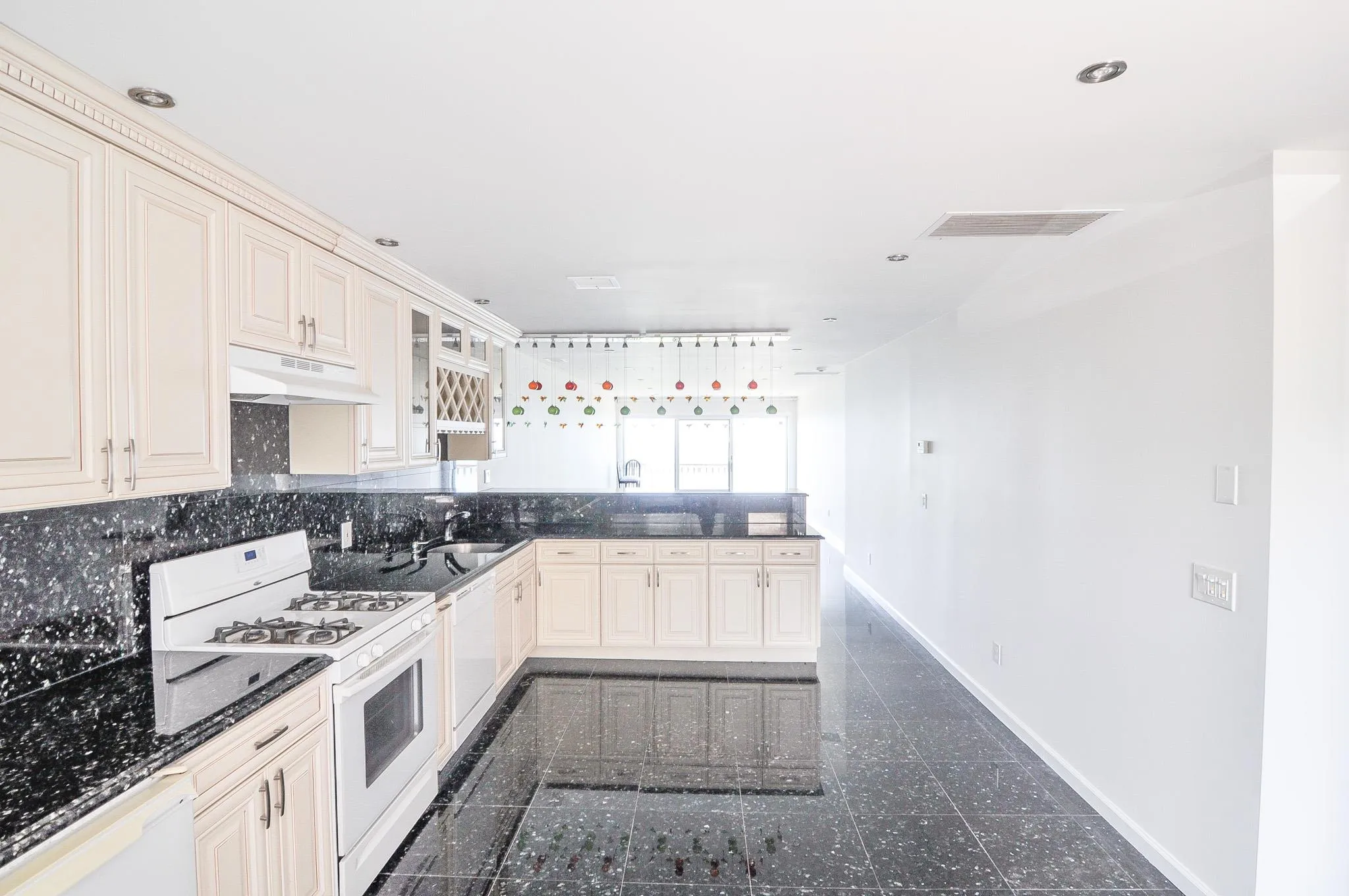 Kitchen with white appliances, under cabinet range hood, granite floors, a peninsula, and decorative backsplash Kitchen with white appliances, under cabinet range hood, granite floors, a peninsula, and decorative backsplash