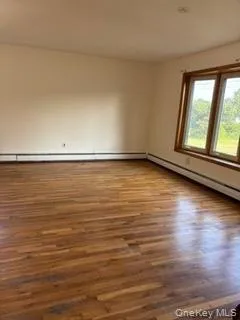 Empty room featuring wood finished floors and baseboard heating Empty room featuring wood finished floors and baseboard heating