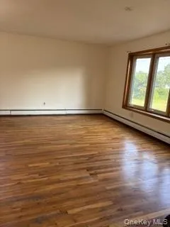 Empty room with wood finished floors and a baseboard heating unit Empty room with wood finished floors and a baseboard heating unit