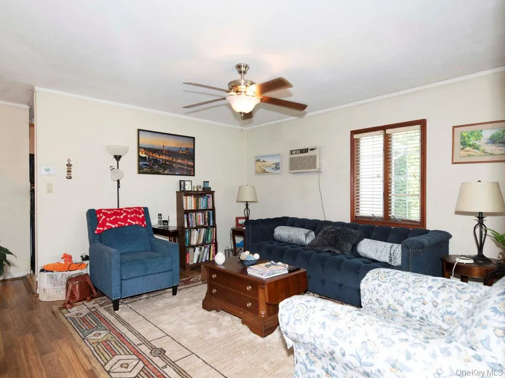 Living room featuring crown molding, ceiling fan, wood finished floors, and a wall mounted air conditioner Living room featuring crown molding, ceiling fan, wood finished floors, and a wall mounted air conditioner