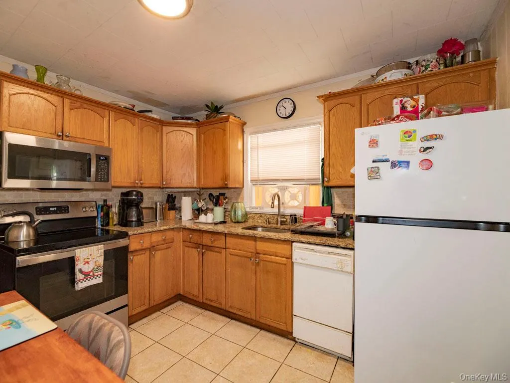 Kitchen featuring appliances with stainless steel finishes, light stone countertops, light tile patterned floors, and brown cabinets Kitchen featuring appliances with stainless steel finishes, light stone countertops, light tile patterned floors, and brown cabinets