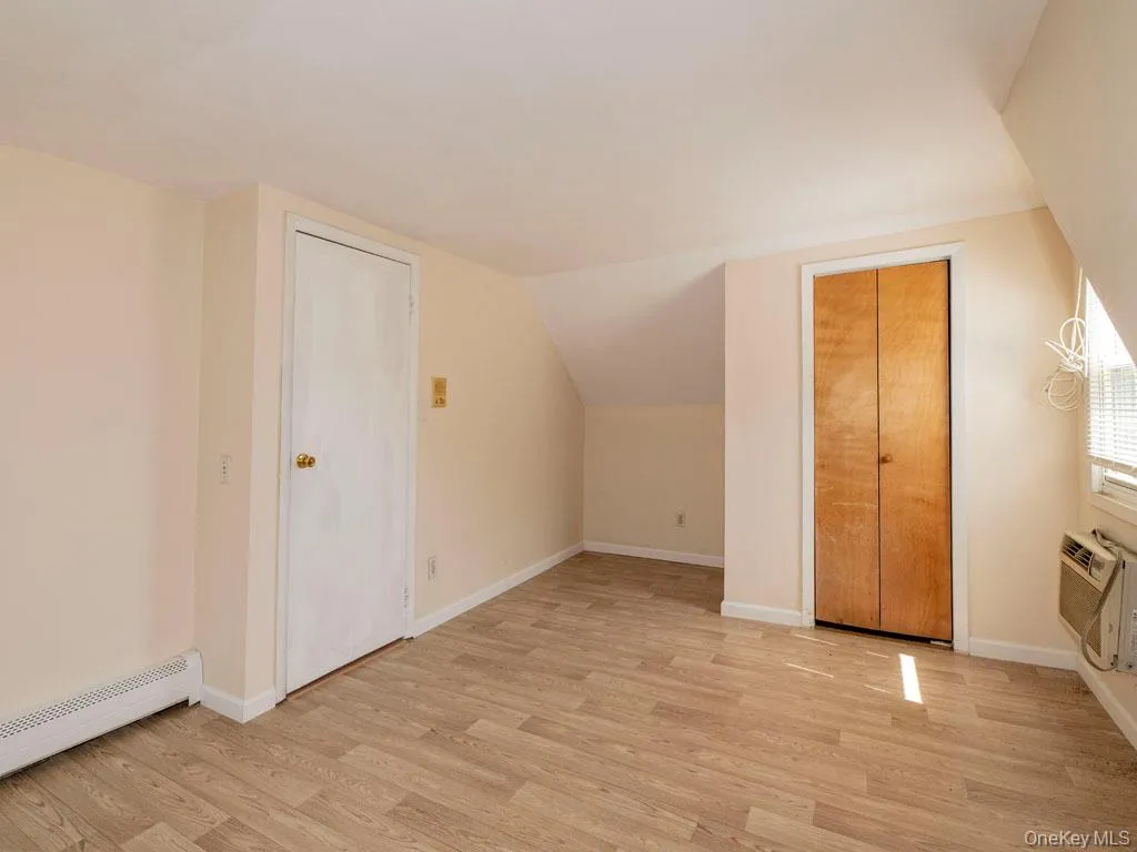Additional living space featuring light wood finished floors, a baseboard radiator, vaulted ceiling, and an AC wall unit Additional living space featuring light wood finished floors, a baseboard radiator, vaulted ceiling, and an AC wall unit