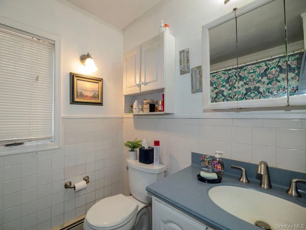 Full bath featuring vanity, crown molding, a baseboard heating unit, tile walls, and a wainscoted wall Full bath featuring vanity, crown molding, a baseboard heating unit, tile walls, and a wainscoted wall