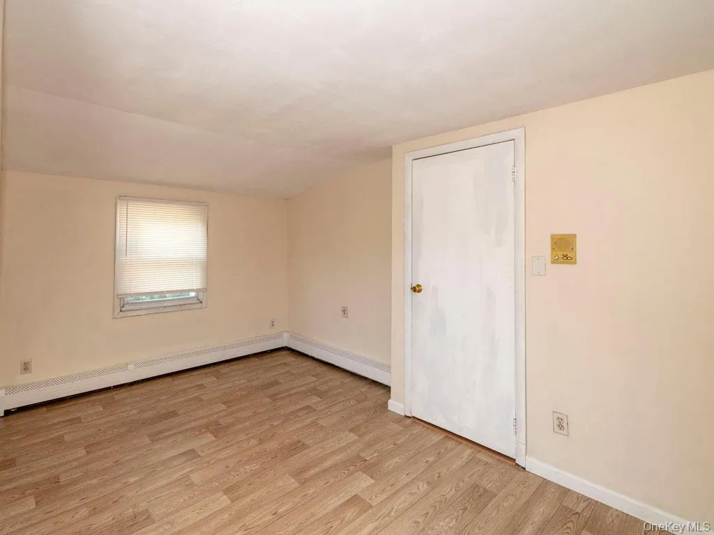 Spare room featuring a baseboard radiator, light wood-style floors, lofted ceiling, and baseboard heating Spare room featuring a baseboard radiator, light wood-style floors, lofted ceiling, and baseboard heating