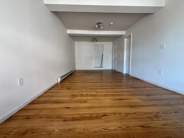 Unfurnished room featuring a baseboard heating unit and wood finished floors Unfurnished room featuring a baseboard heating unit and wood finished floors