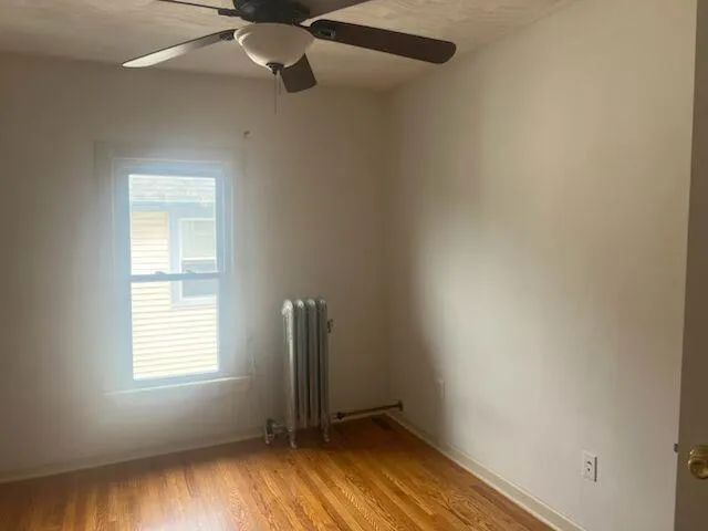 Unfurnished room with light wood-style flooring, radiator heating unit, and a ceiling fan Unfurnished room with light wood-style flooring, radiator heating unit, and a ceiling fan