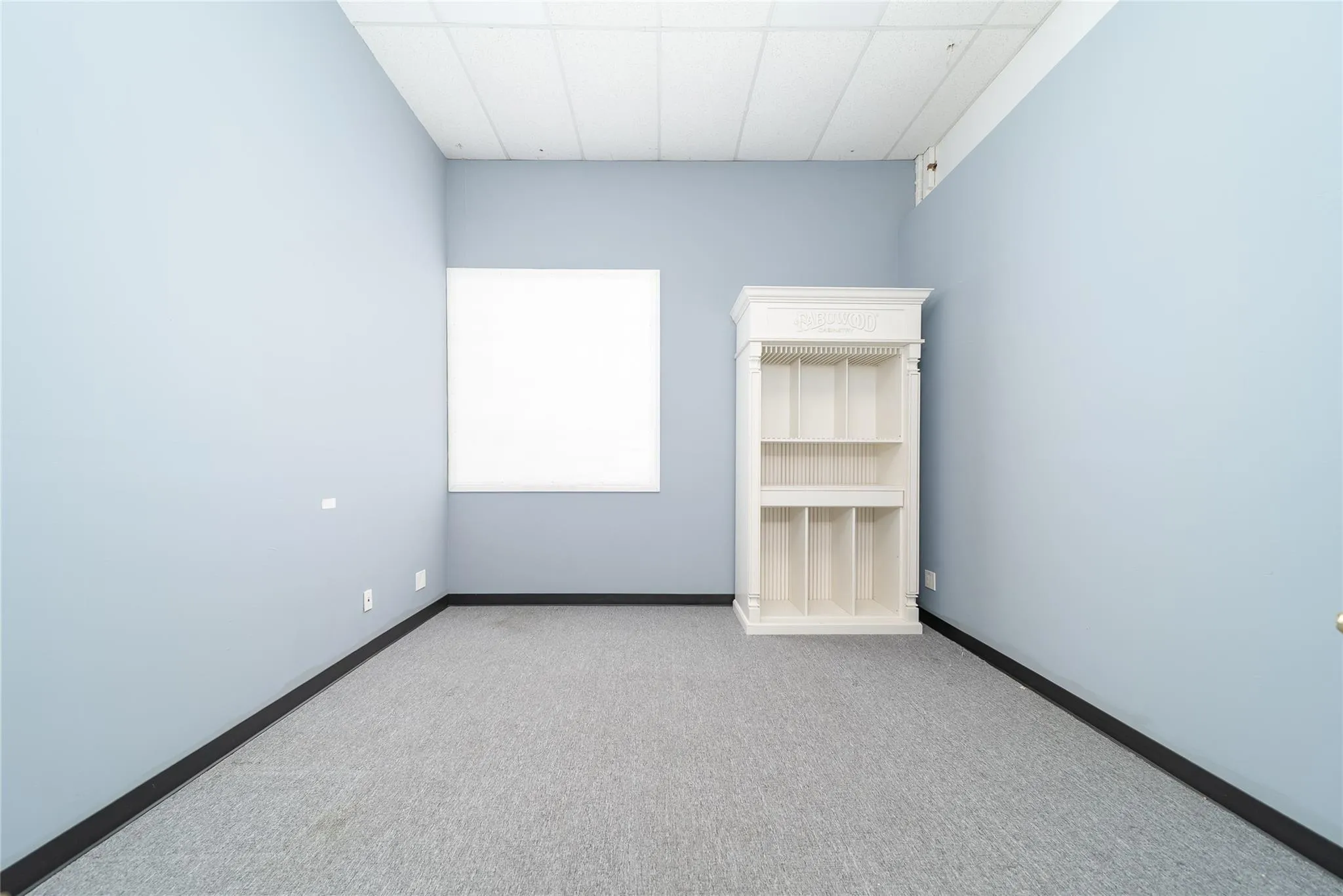 Carpeted empty room with a paneled ceiling and baseboards Carpeted empty room with a paneled ceiling and baseboards