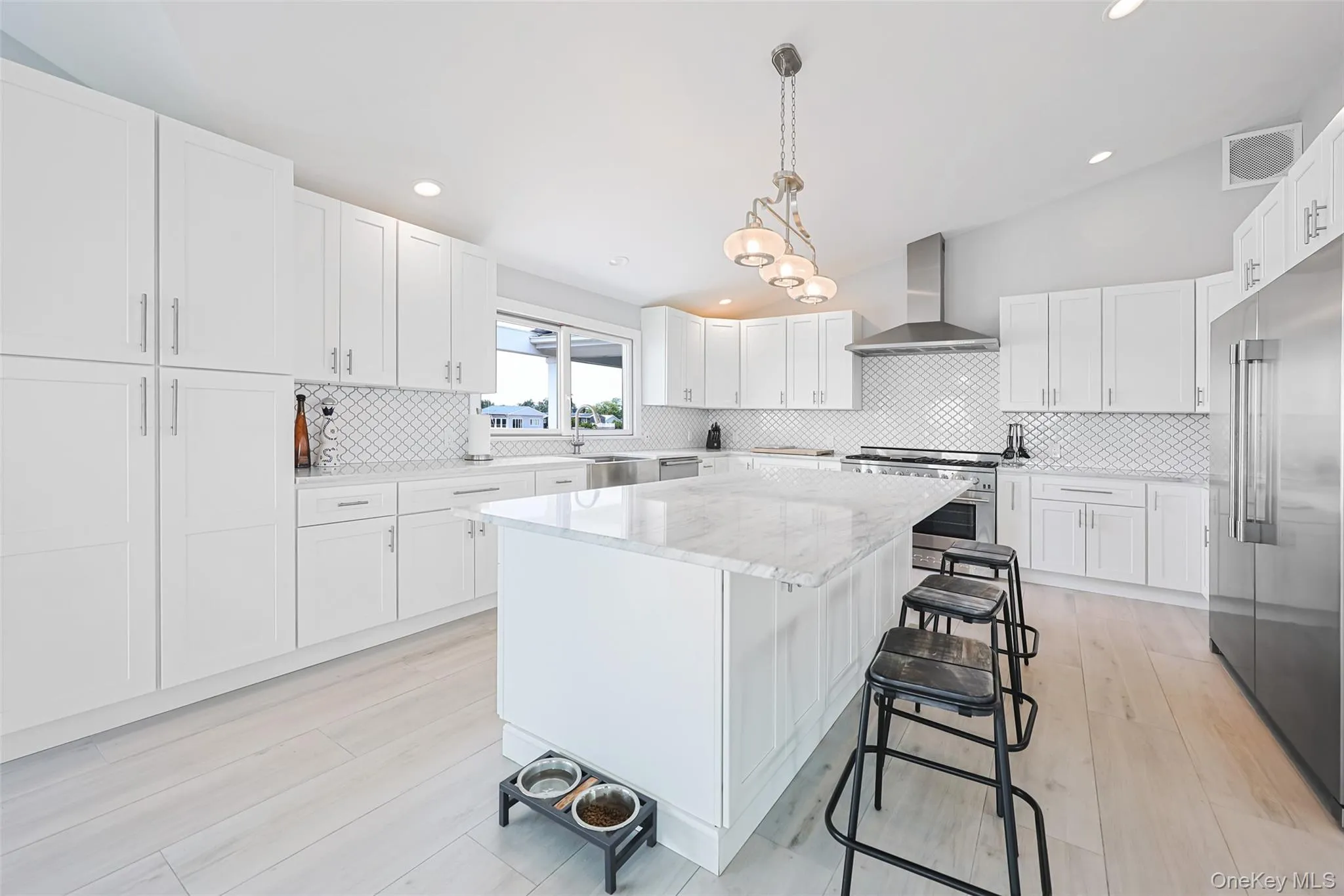 Kitchen featuring wall chimney range hood, premium appliances, a kitchen island, a breakfast bar area, and backsplash Kitchen featuring wall chimney range hood, premium appliances, a kitchen island, a breakfast bar area, and backsplash