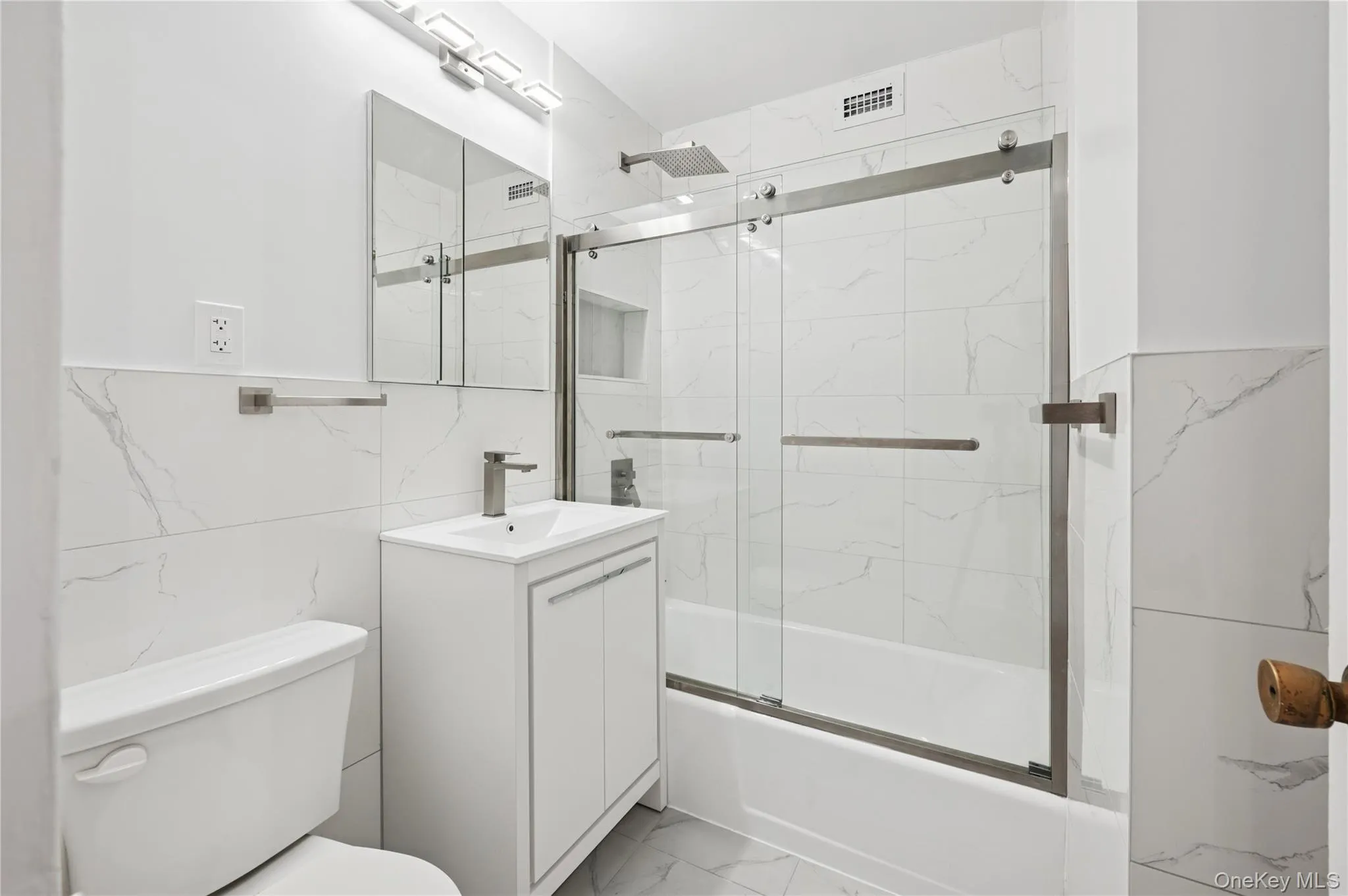 Full bathroom with marble look tiles, vanity, tile walls, and bath / shower combo with glass door Full bathroom with marble look tiles, vanity, tile walls, and bath / shower combo with glass door