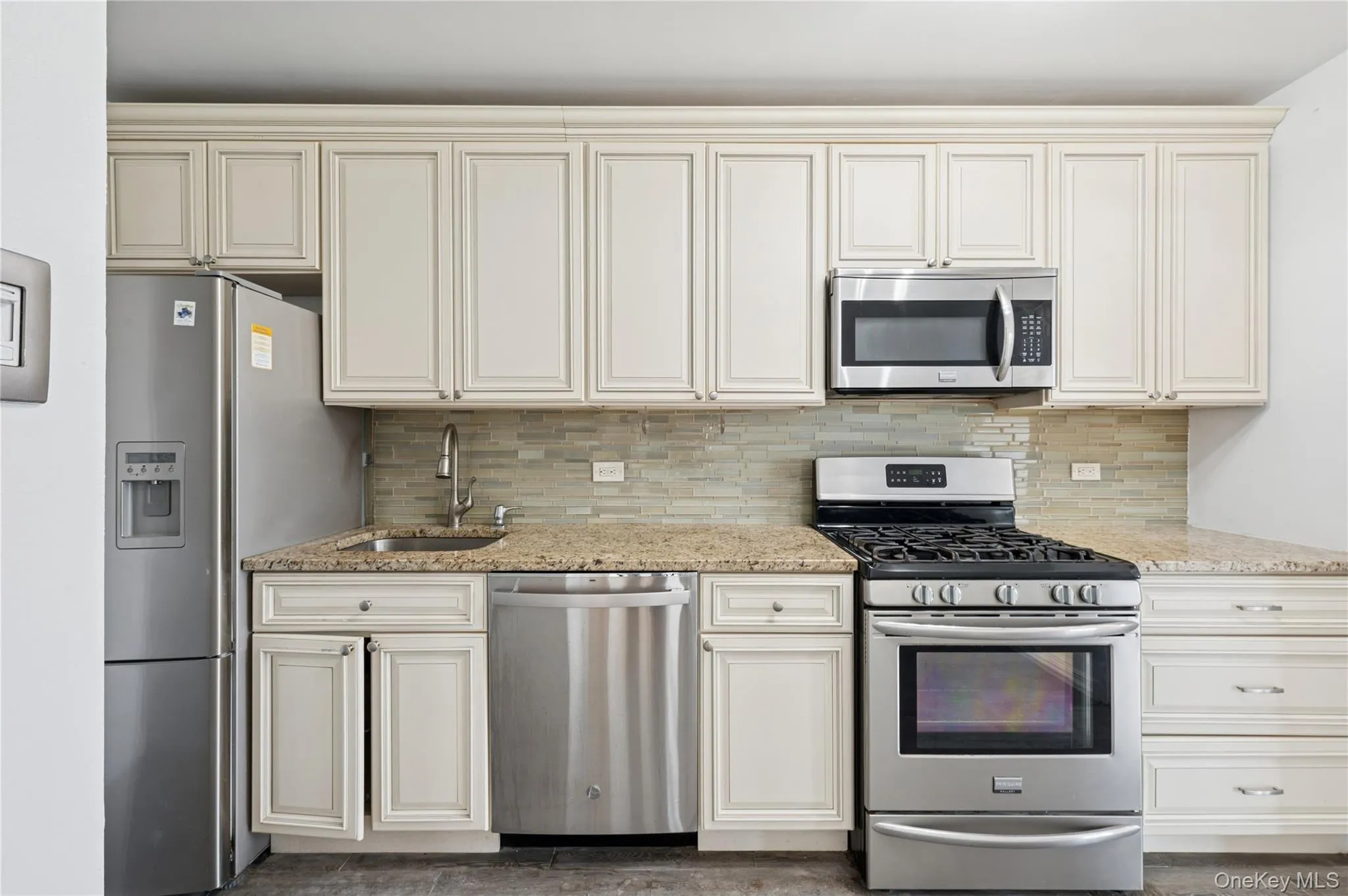 Kitchen with appliances with stainless steel finishes, light stone counters, tasteful backsplash, and cream cabinets Kitchen with appliances with stainless steel finishes, light stone counters, tasteful backsplash, and cream cabinets