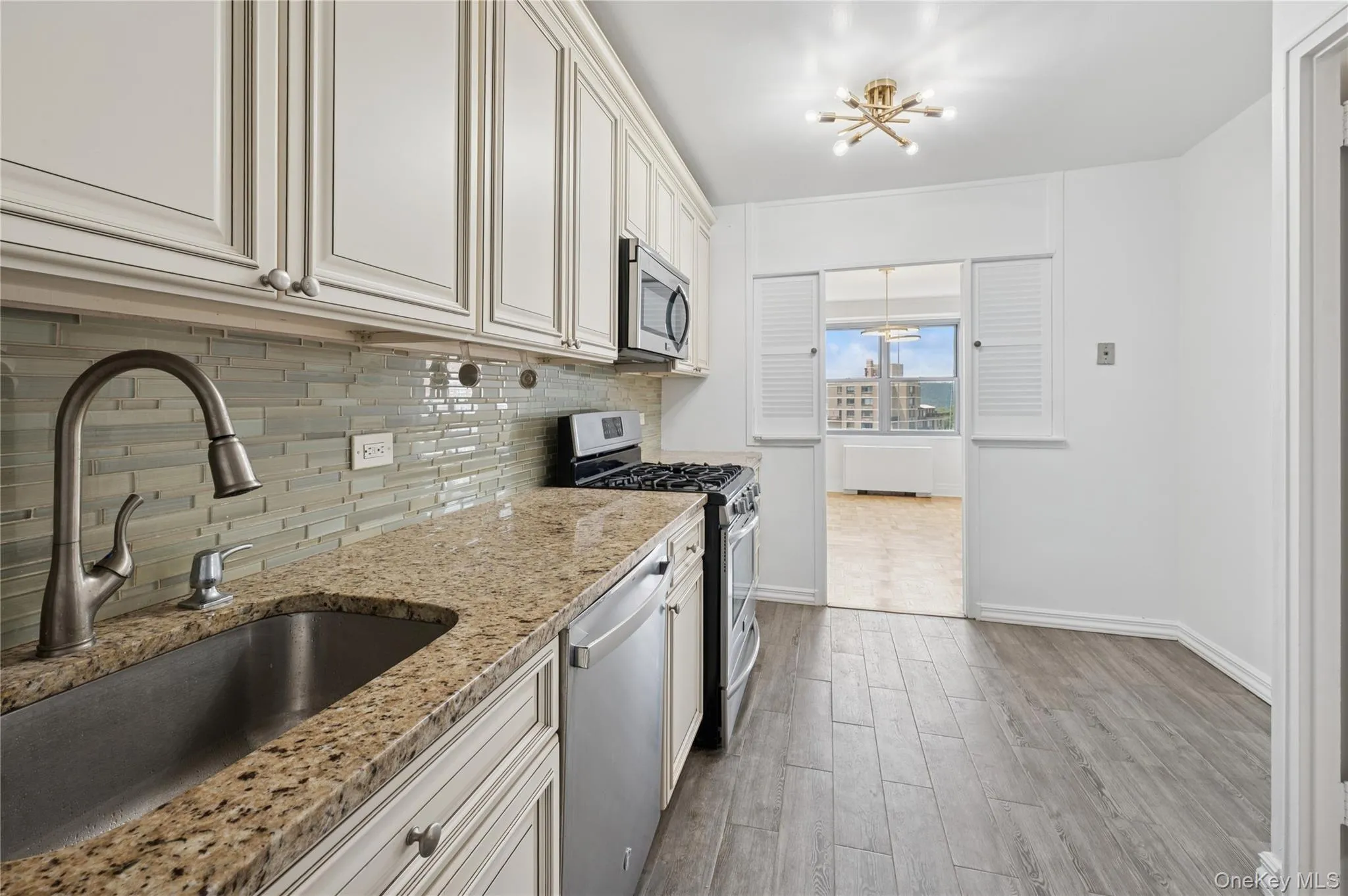 Kitchen featuring stainless steel appliances, a chandelier, backsplash, light wood-type flooring, and light stone countertops Kitchen featuring stainless steel appliances, a chandelier, backsplash, light wood-type flooring, and light stone countertops