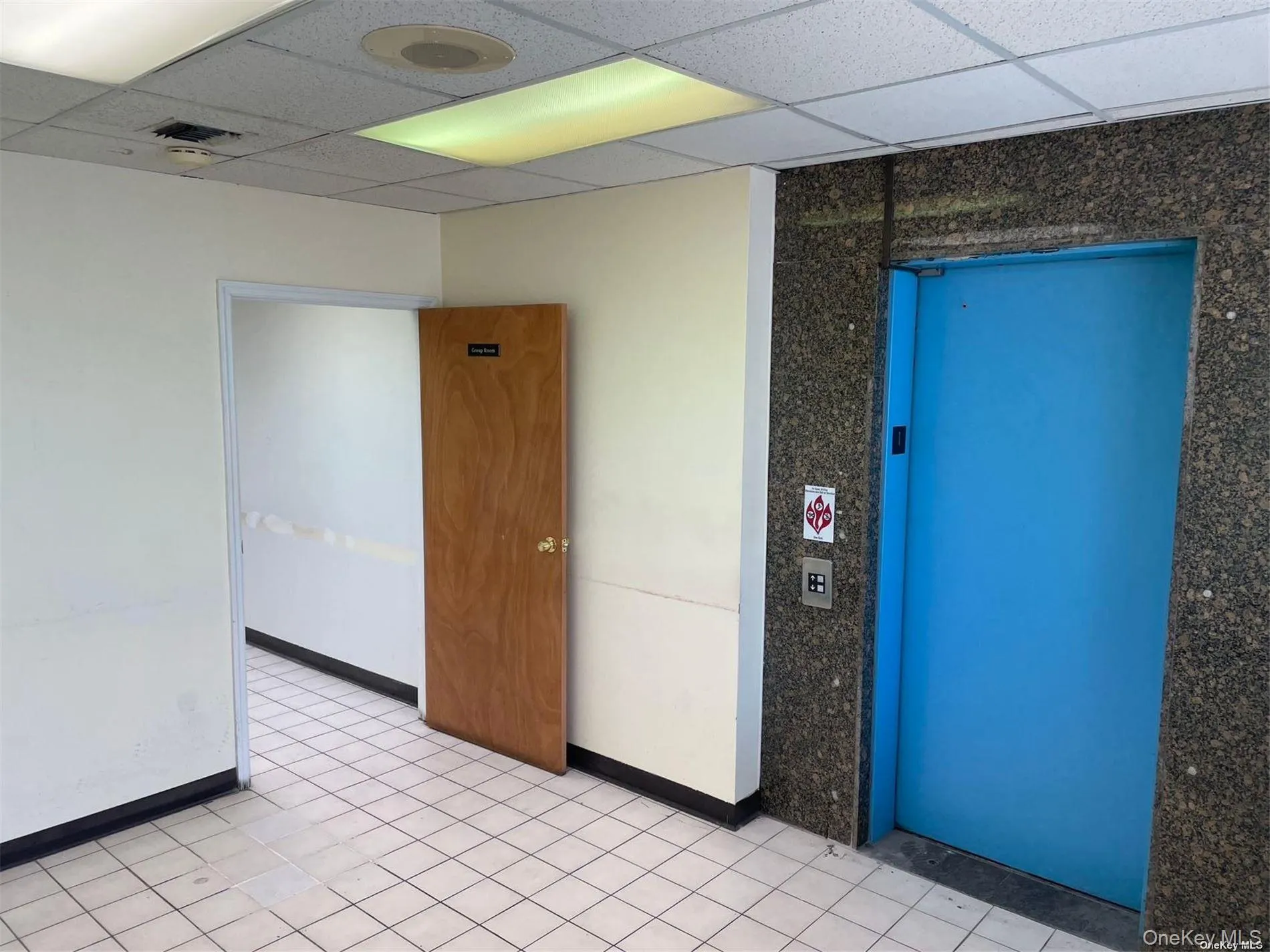 Spare room featuring a drop ceiling, elevator, and light tile patterned floors Spare room featuring a drop ceiling, elevator, and light tile patterned floors