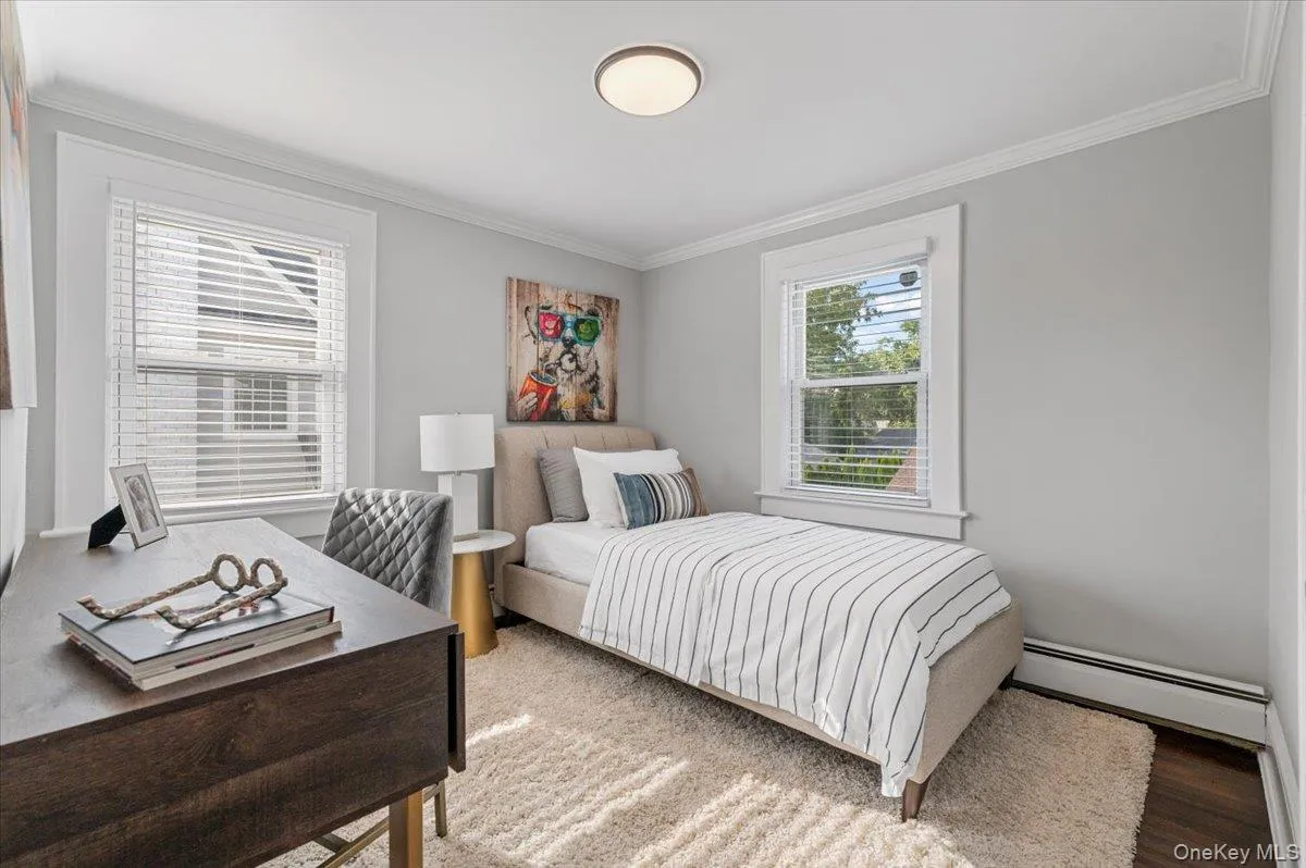 Bedroom featuring ornamental molding, a baseboard radiator, wood finished floors, and a desk Bedroom featuring ornamental molding, a baseboard radiator, wood finished floors, and a desk