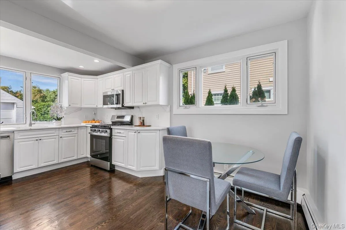 Kitchen with white cabinets, appliances with stainless steel finishes, dark wood-style floors, a baseboard heating unit, and recessed lighting Kitchen with white cabinets, appliances with stainless steel finishes, dark wood-style floors, a baseboard heating unit, and recessed lighting