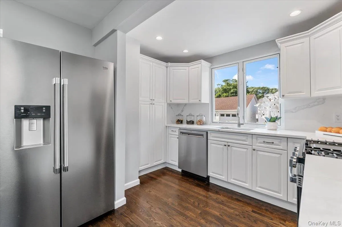Kitchen featuring appliances with stainless steel finishes, white cabinetry, dark wood-style flooring, light stone counters, and recessed lighting Kitchen featuring appliances with stainless steel finishes, white cabinetry, dark wood-style flooring, light stone counters, and recessed lighting