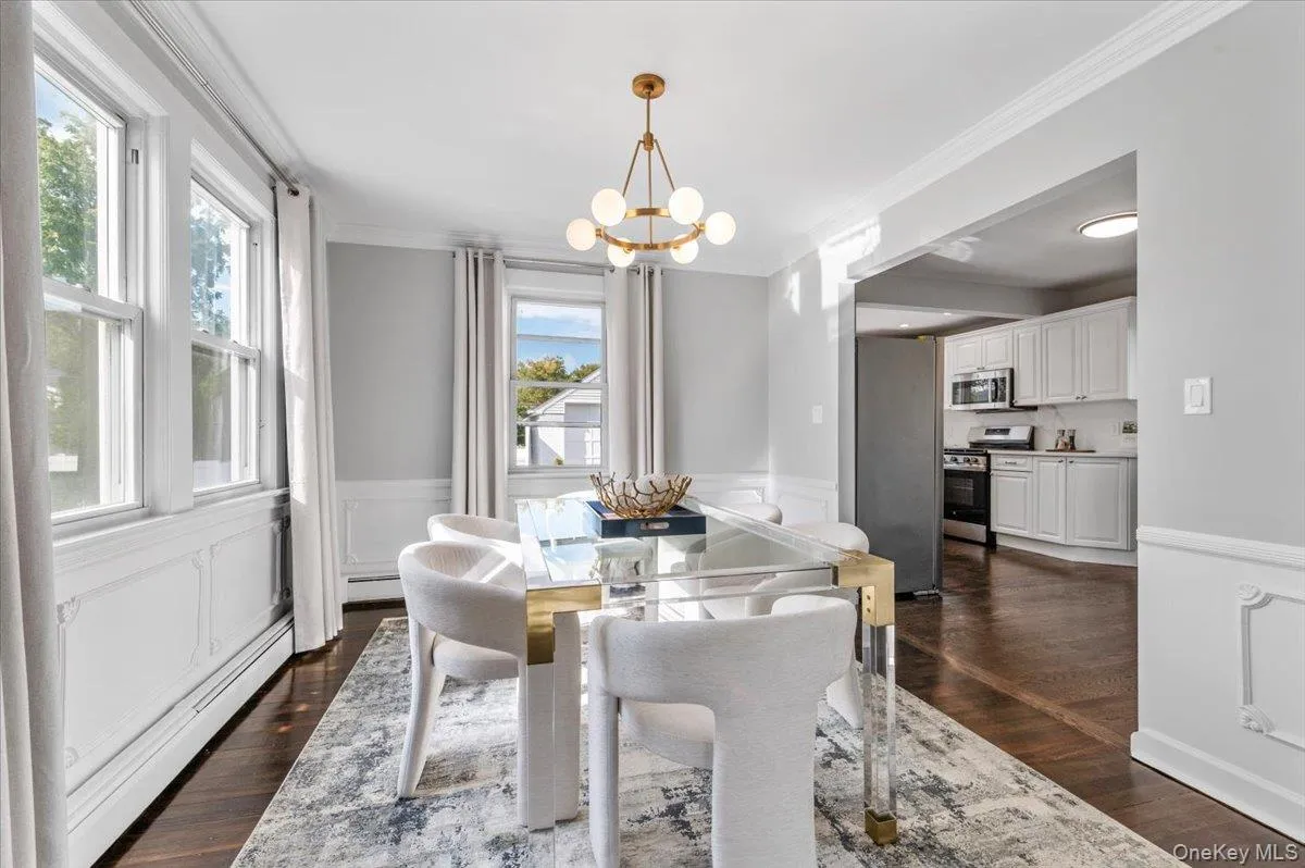 Dining room featuring crown molding, wainscoting, a decorative wall, dark wood-type flooring, and a chandelier Dining room featuring crown molding, wainscoting, a decorative wall, dark wood-type flooring, and a chandelier