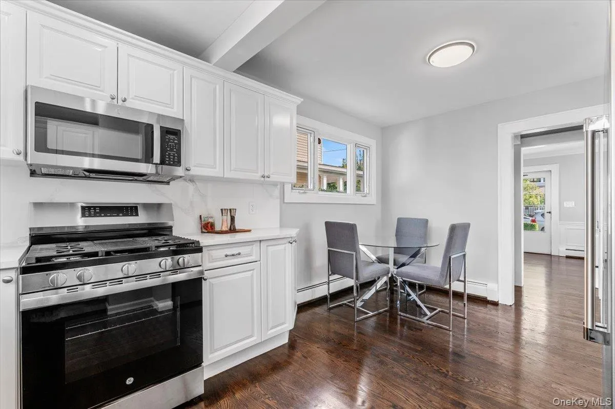 Kitchen with stainless steel appliances, white cabinetry, dark wood-style flooring, a baseboard radiator, and light stone counters Kitchen with stainless steel appliances, white cabinetry, dark wood-style flooring, a baseboard radiator, and light stone counters