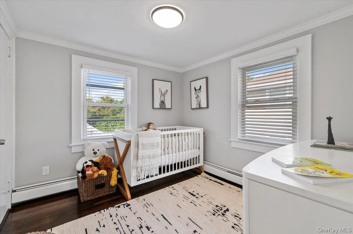 Bedroom with ornamental molding, wood finished floors, multiple windows, baseboard heating, and a nursery area Bedroom with ornamental molding, wood finished floors, multiple windows, baseboard heating, and a nursery area