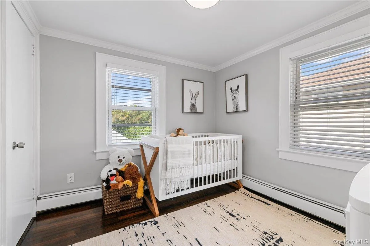 Bedroom featuring a baseboard heating unit, ornamental molding, a nursery area, and wood finished floors Bedroom featuring a baseboard heating unit, ornamental molding, a nursery area, and wood finished floors