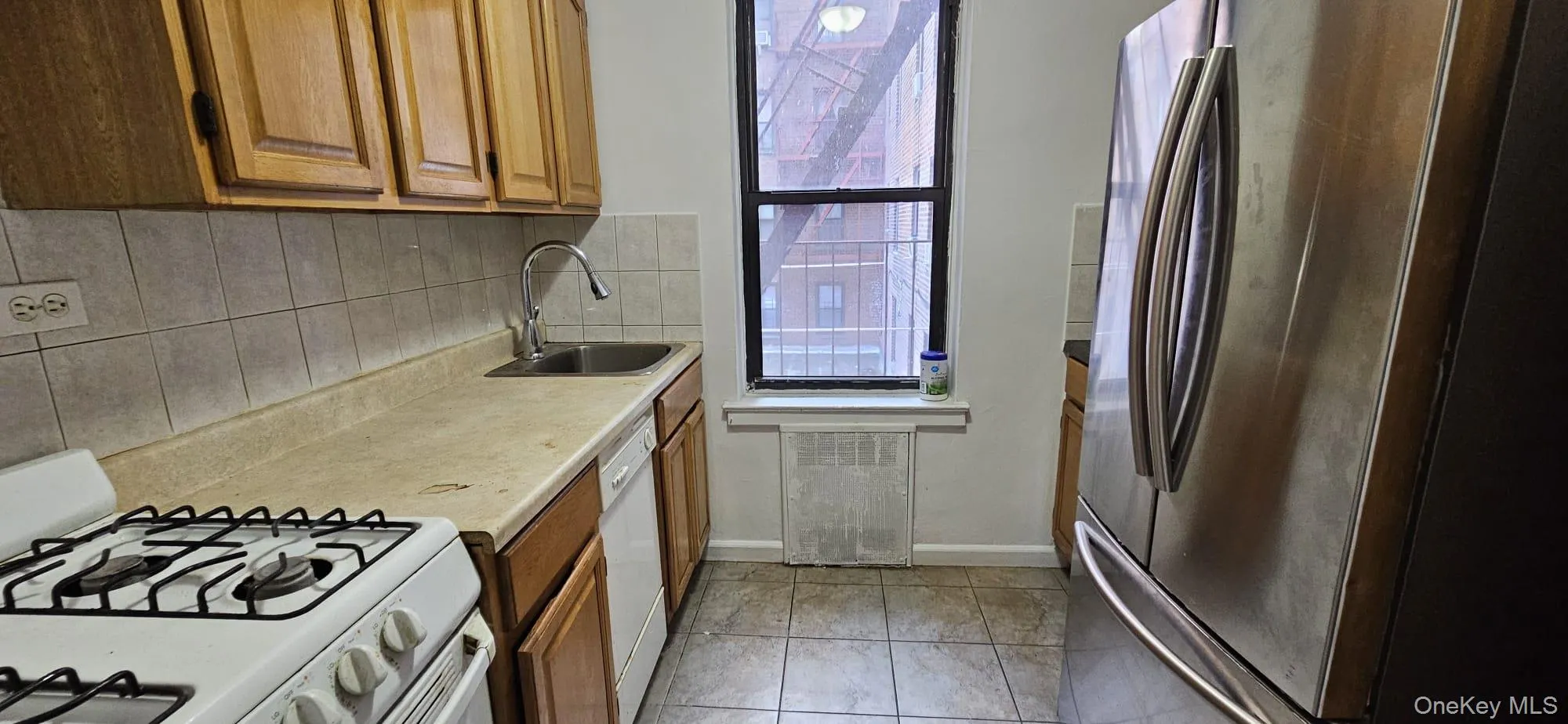 Kitchen with white appliances, tasteful backsplash, light countertops, brown cabinets, and light tile patterned floors Kitchen with white appliances, tasteful backsplash, light countertops, brown cabinets, and light tile patterned floors