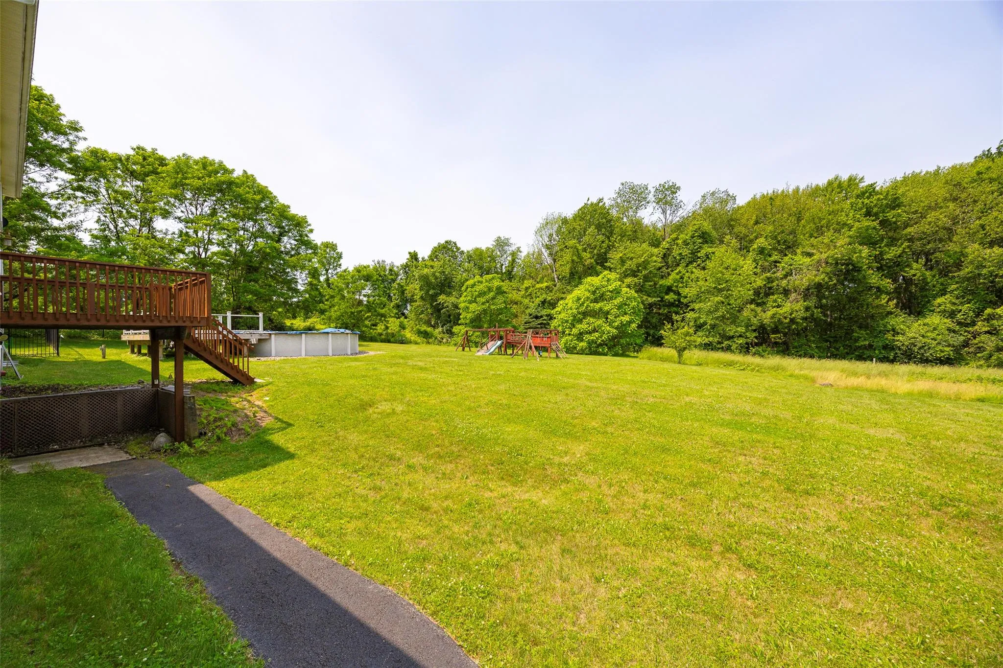 View of green lawn featuring a playground, a wooden deck, an outdoor pool, and stairway View of green lawn featuring a playground, a wooden deck, an outdoor pool, and stairway