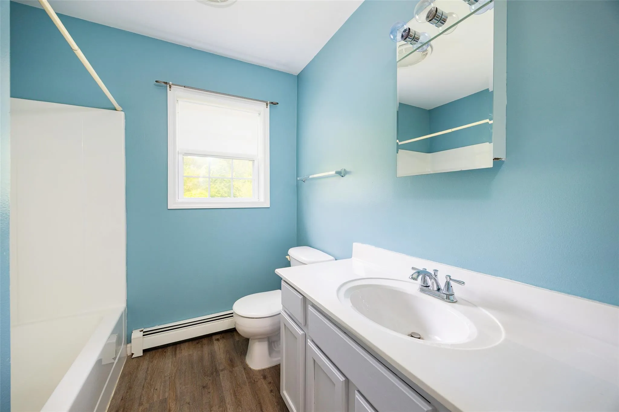 Full bathroom with a baseboard heating unit, wood finished floors, vanity, and shower / bath combination Full bathroom with a baseboard heating unit, wood finished floors, vanity, and shower / bath combination