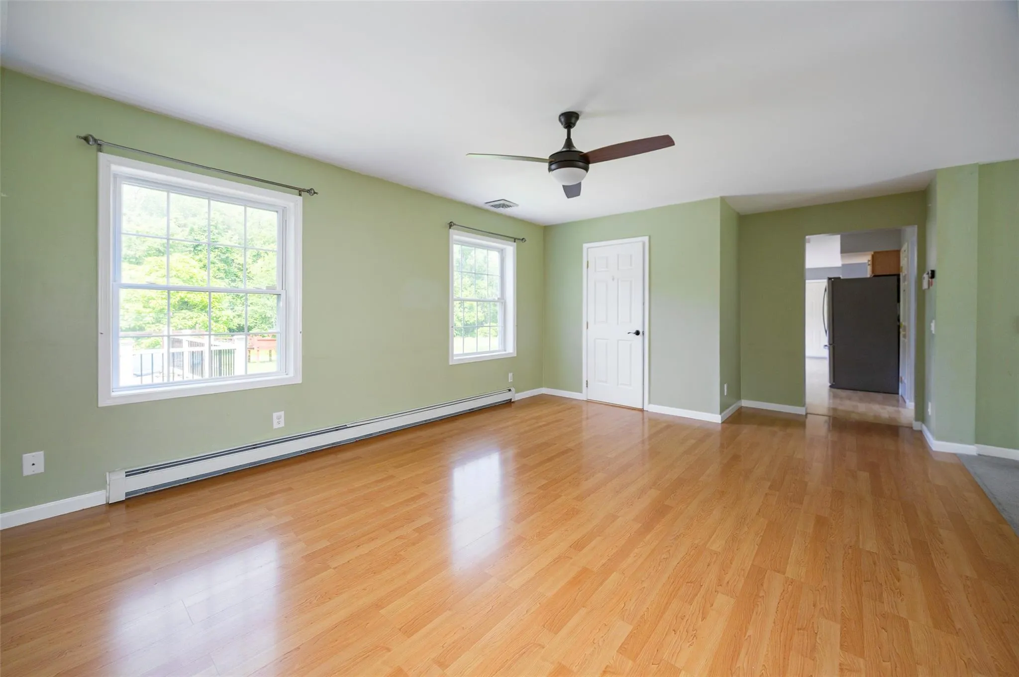 Unfurnished room featuring baseboard heating, ceiling fan, and light wood finished floors Unfurnished room featuring baseboard heating, ceiling fan, and light wood finished floors