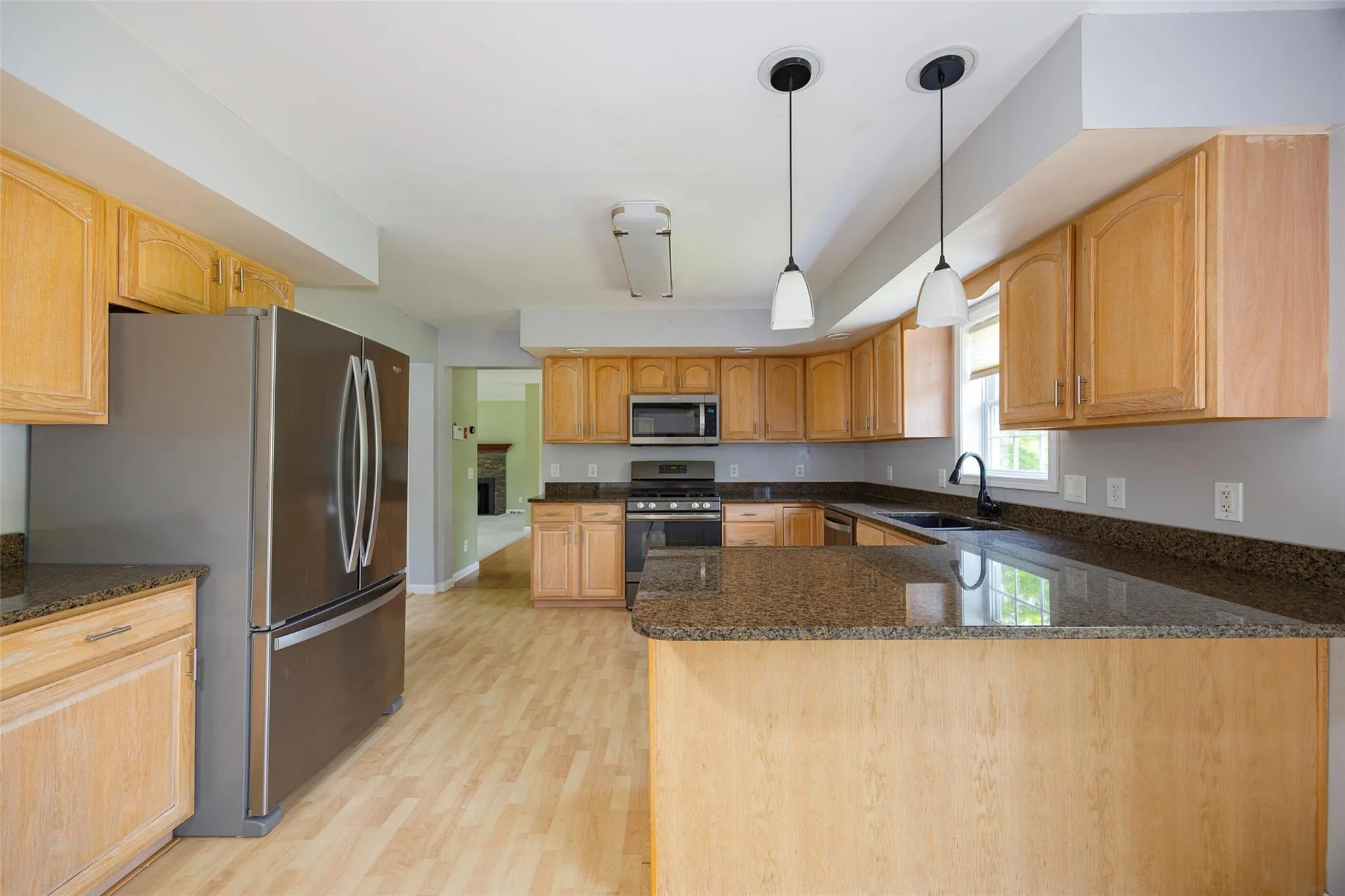 Kitchen with appliances with stainless steel finishes, light wood finished floors, dark stone counters, a peninsula, and decorative light fixtures Kitchen with appliances with stainless steel finishes, light wood finished floors, dark stone counters, a peninsula, and decorative light fixtures