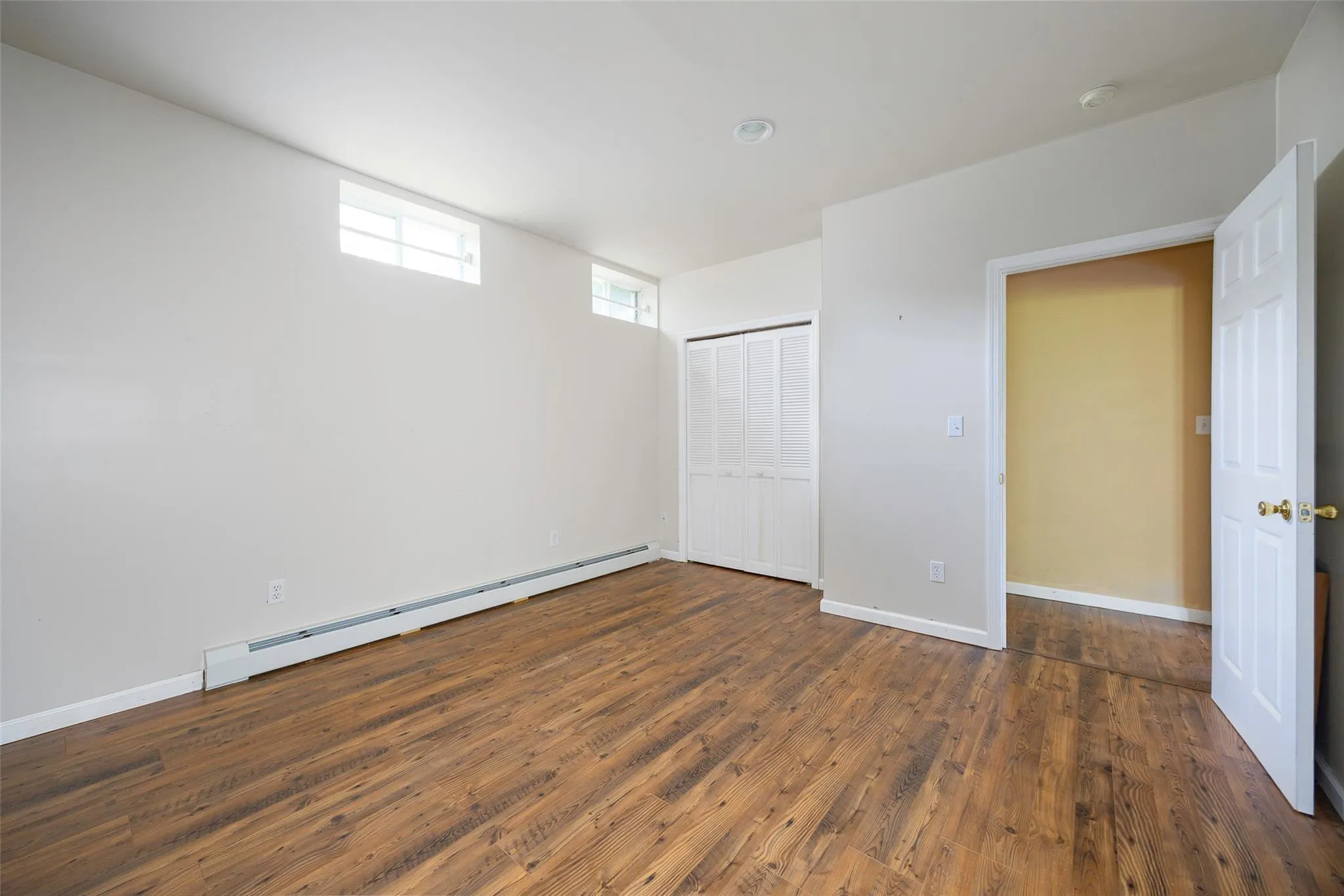 Unfurnished bedroom featuring baseboard heating, wood finished floors, and a closet Unfurnished bedroom featuring baseboard heating, wood finished floors, and a closet