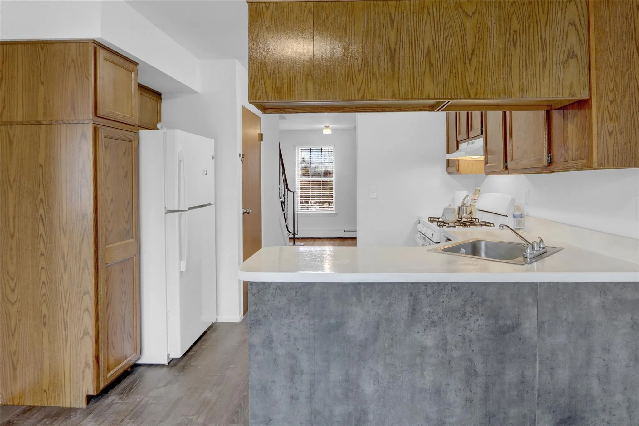 Kitchen with white appliances, under cabinet range hood, a peninsula, light countertops, and wood finished floors Kitchen with white appliances, under cabinet range hood, a peninsula, light countertops, and wood finished floors